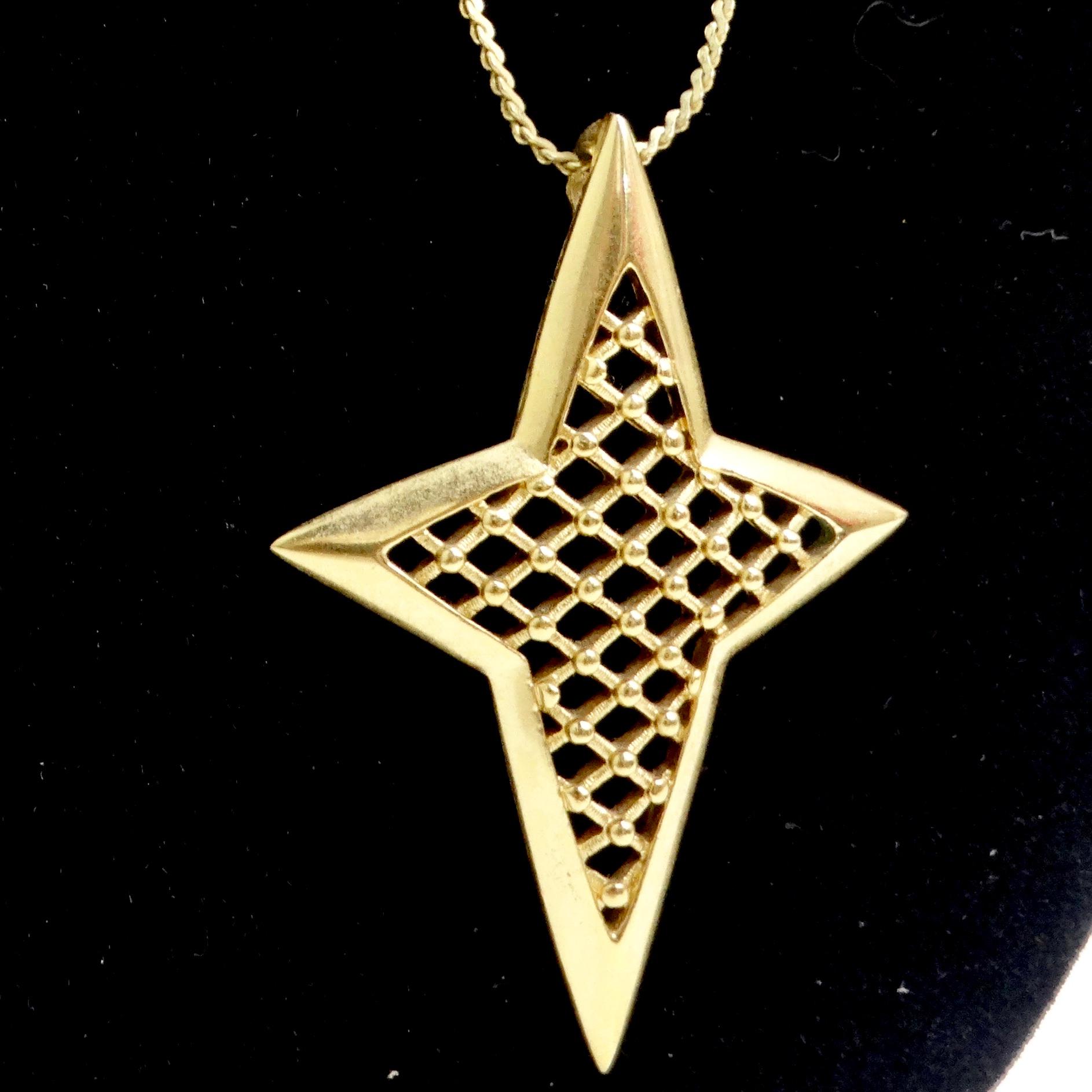 Introducing the Trifari Gold Tone Star Pendant Necklace – a classic piece that adds a touch of celestial elegance to your style! This exquisite gold tone necklace features a large star-shaped pendant with a captivating crisscross design, reminiscent