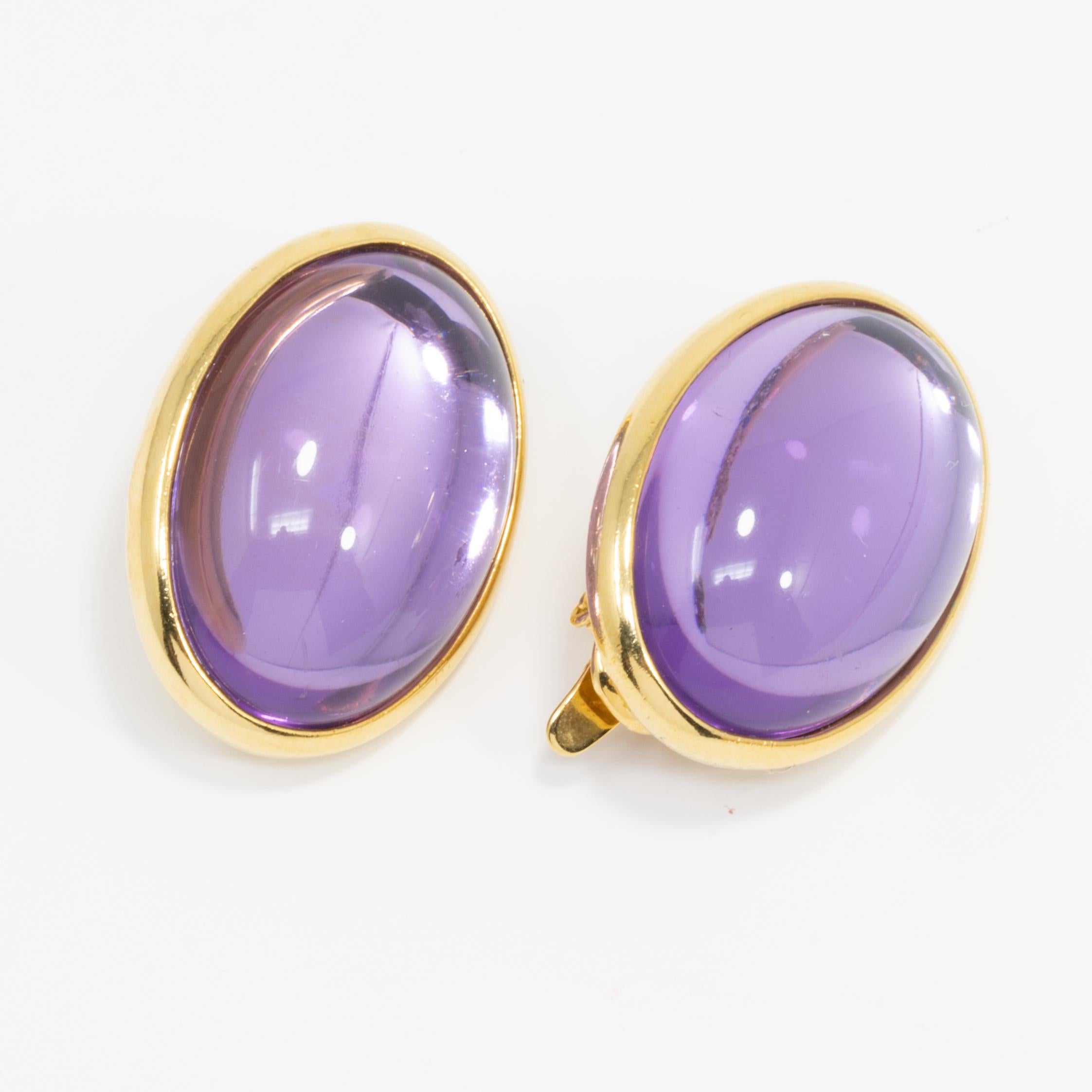 A pair of retro-style Trifari clip-on earrings. Translucent, moon-glow, amethyst cabochons are set in oval, gold-plated clips for a sophisticated, mysterious look.

Hallmarks: Trifari TM