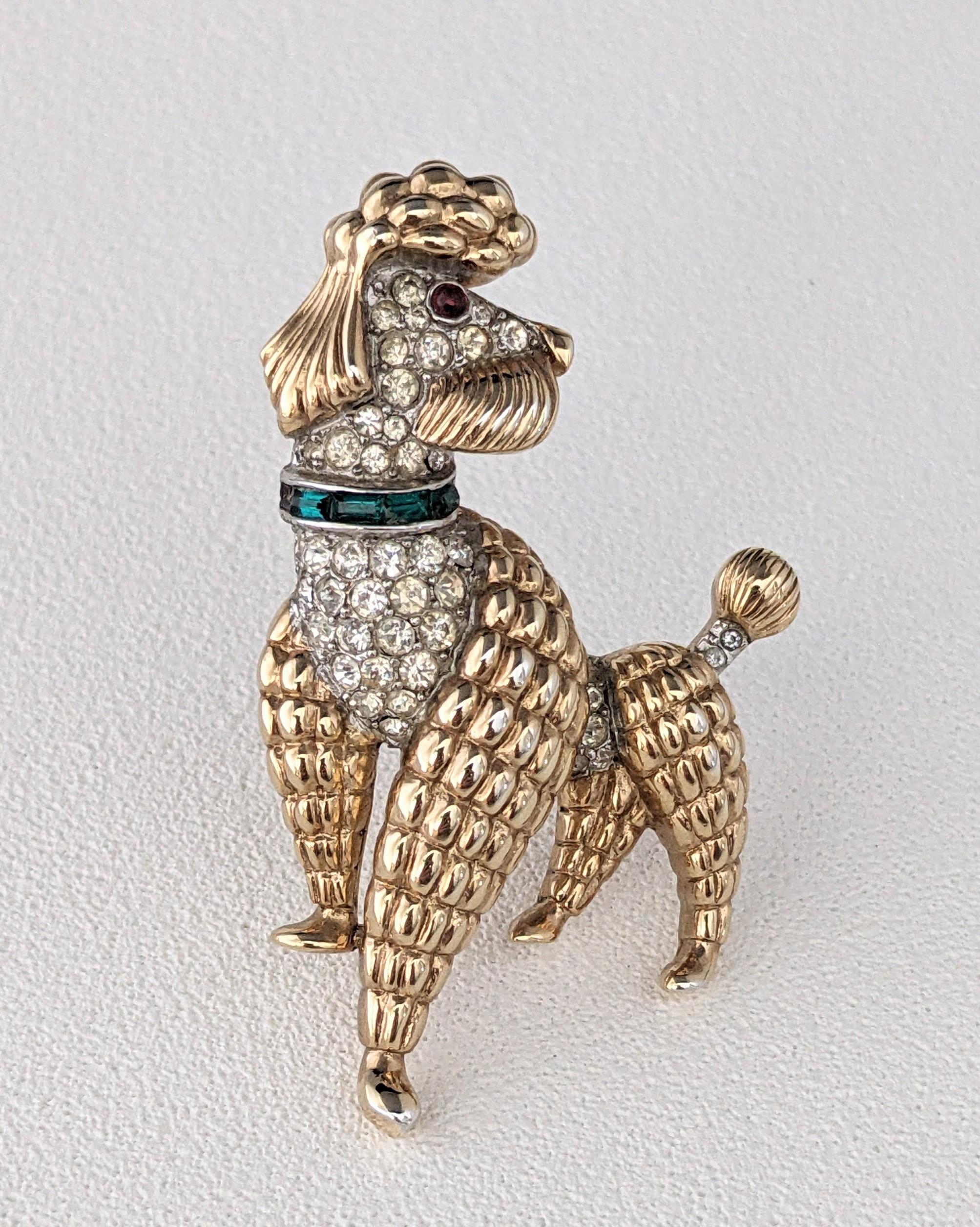 Charming Trifari Mid Century Poodle Brooch from the 1950's. Gilt poodle with pave accents with emerald baguette collar and faux ruby cab eye. This design comes from Trifari's 