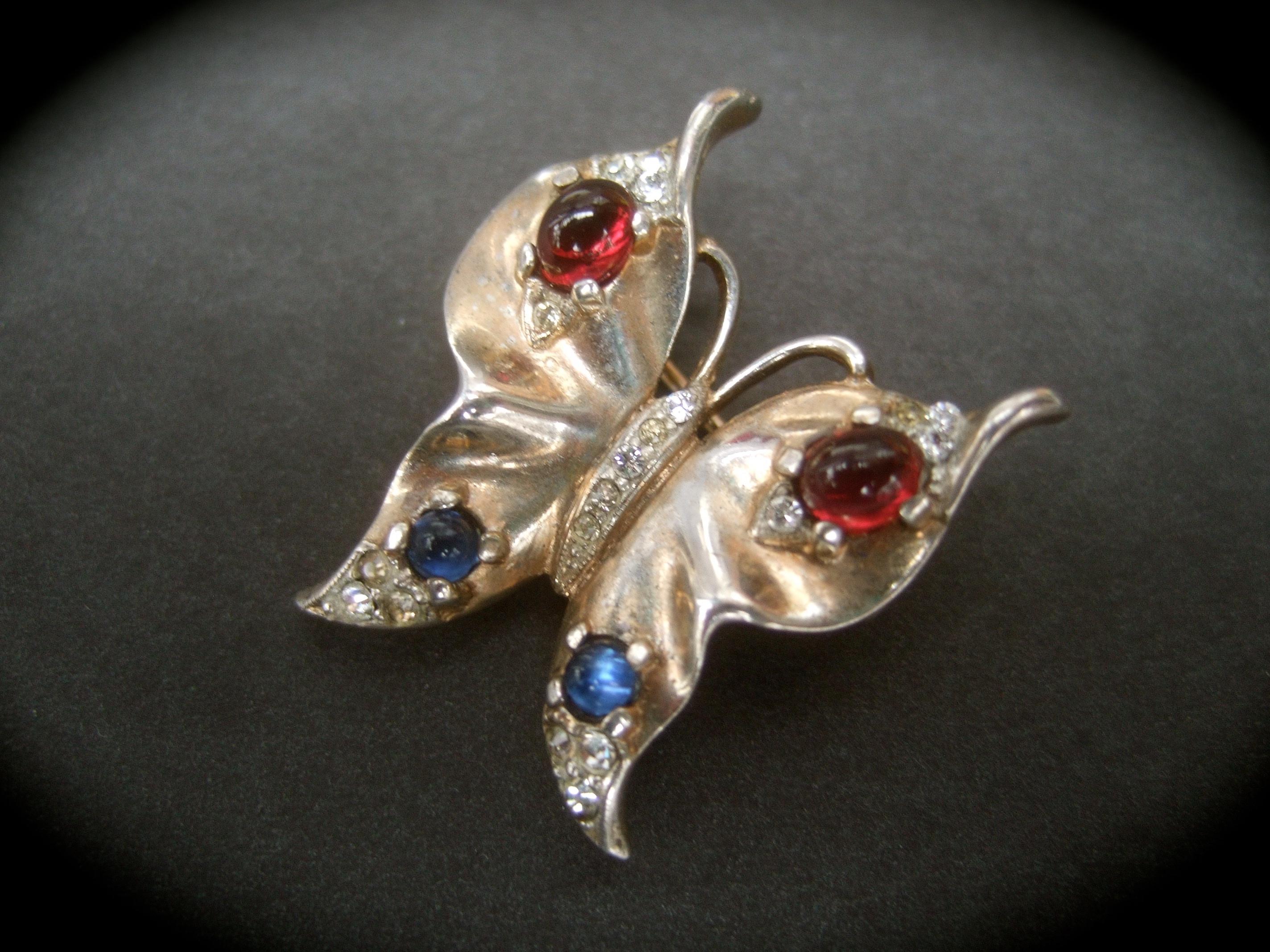 Trifari 1940s Sterling vermeil diminutive butterfly brooch 
The elegant small scale brooch is embellished with ruby color and sapphire blue glass cabochons 

Sheathed in gilt vermeil; accented with tiny clusters of diamante pave' crystals 
The