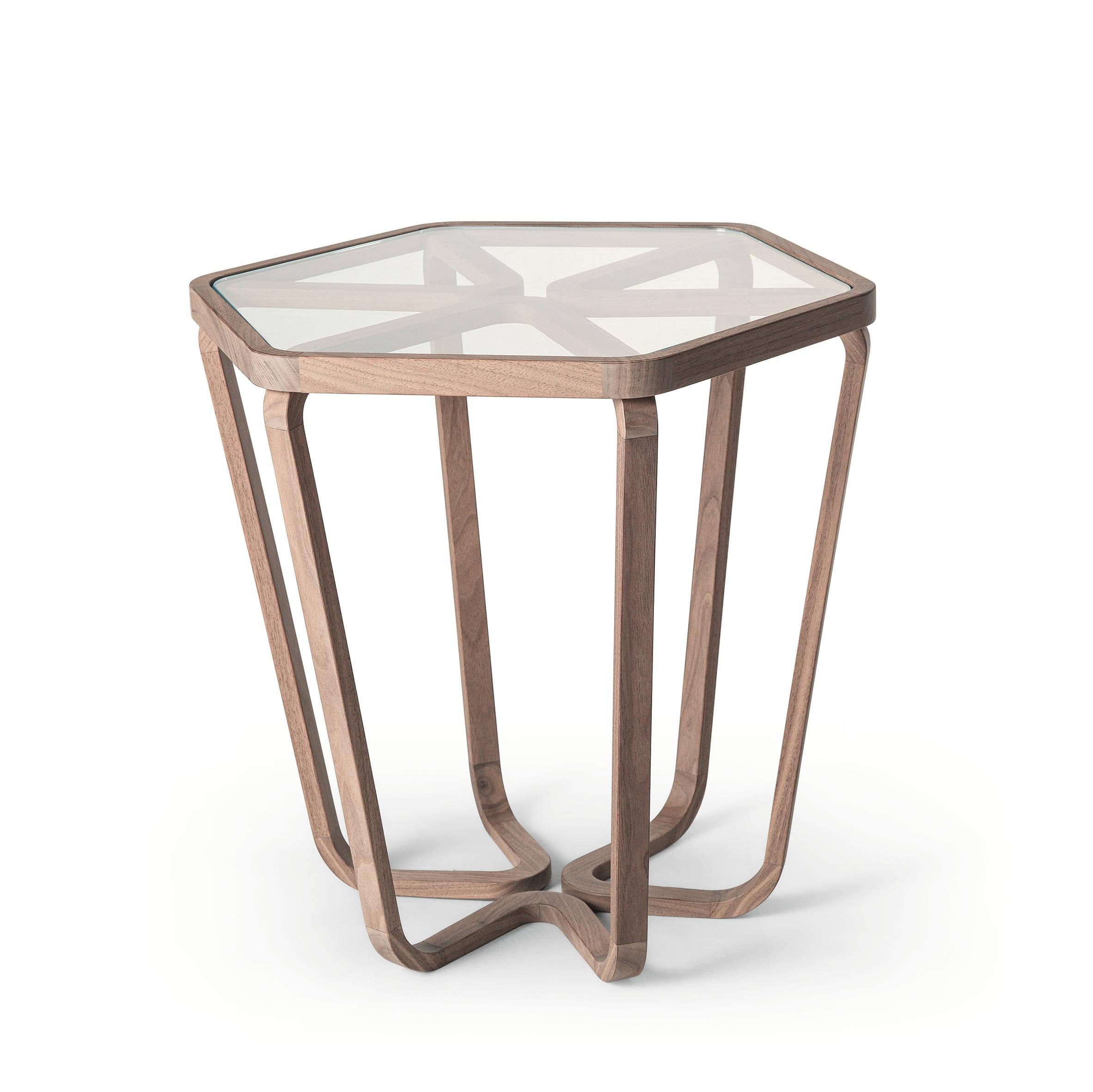 Trifolio est une table basse de forme hexagonale composée d'une structure en bois de noyer massif et d'angles arrondis. Les jambes divergentes créent une illusion de dynamisme qui change selon le point de vue de l'observateur. Les sections des