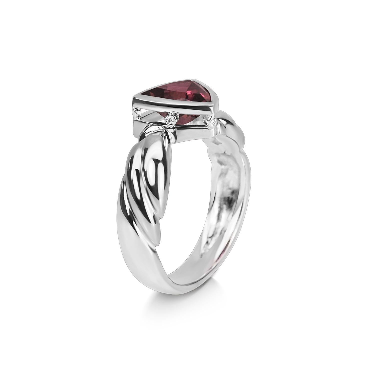 This trillion cut pink tourmaline ring is made in 18ct White Gold with a carved style band. The pink tourmaline is a beautiful faceted deep smokey pink colour and is held in a rubover style setting. The setting has the extra detail of small diamonds