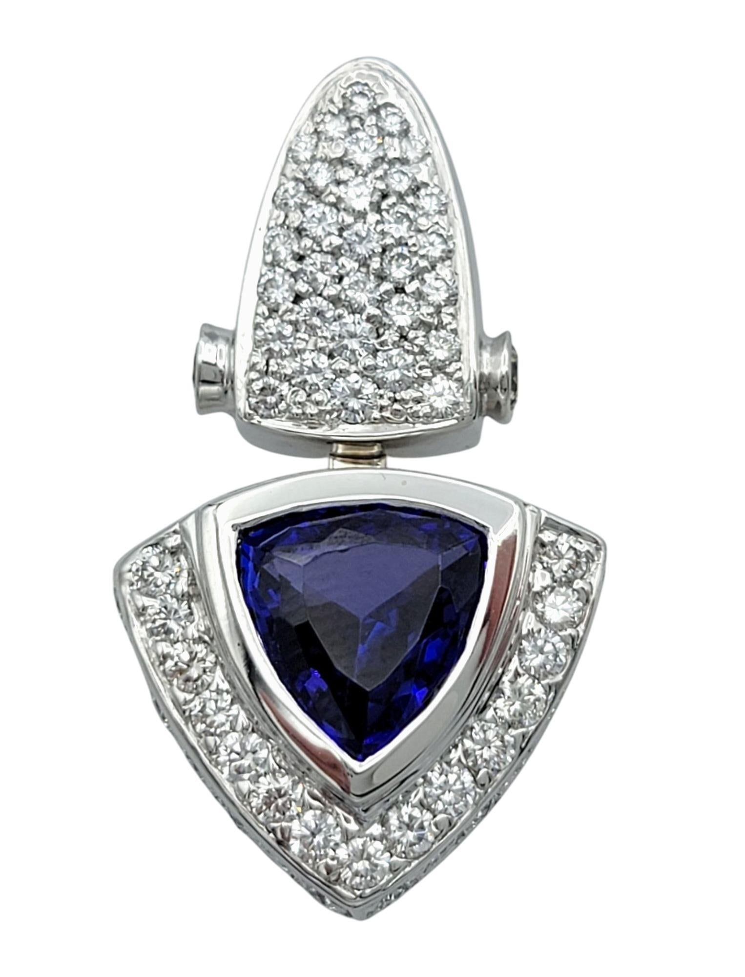 These exquisite earrings feature striking trillion-cut tanzanites in a stunning blue hue, elegantly set in 18 karat white gold. The captivating tanzanites are framed by a shimmering halo of round-cut diamonds, enhancing their brilliance and adding a