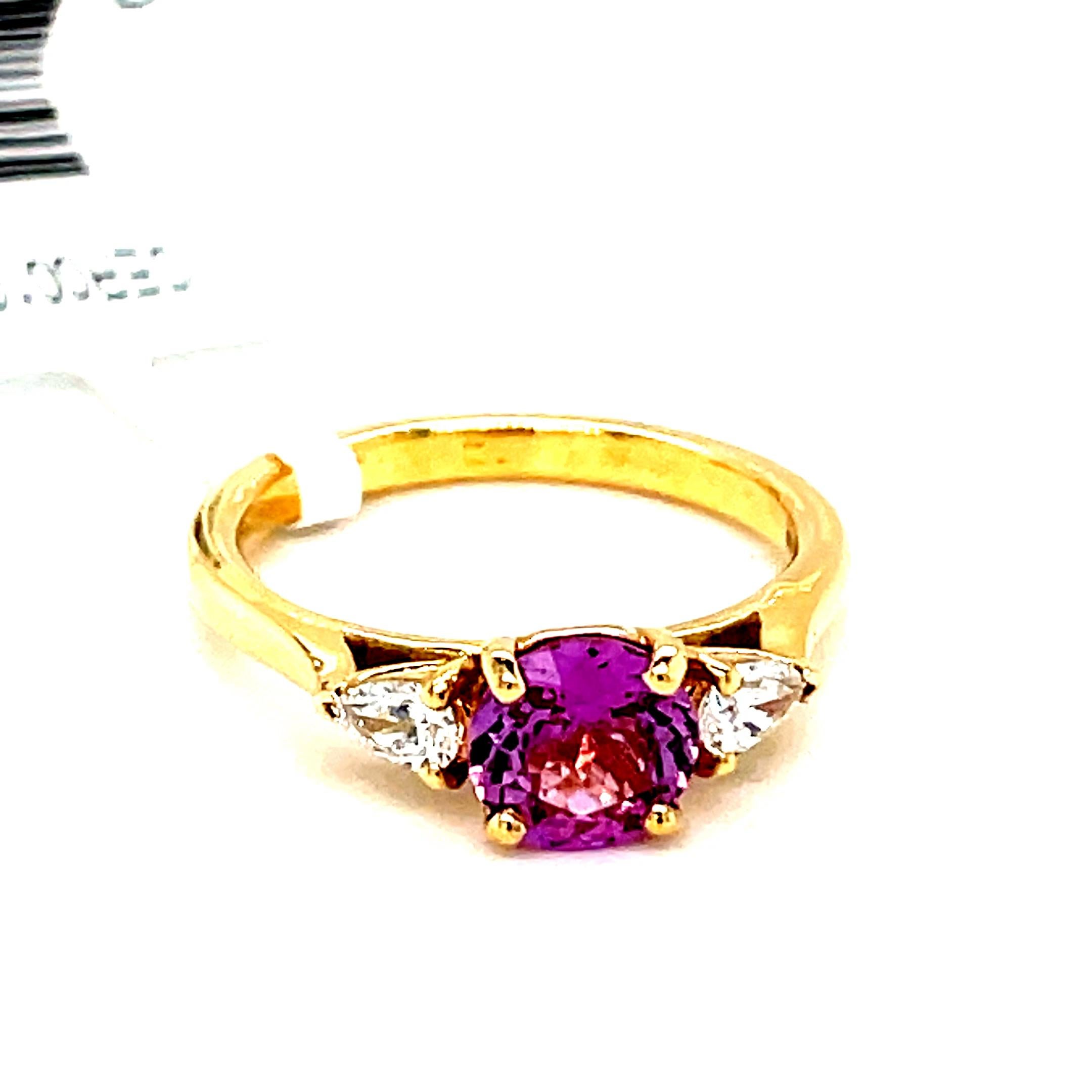This exquisite engagement ring is crafted from 18-karat yellow gold and features a captivating pink sapphire and two sparkling diamonds.

The centerpiece of the ring is a stunning, round-cut pink sapphire. This vibrant gemstone is securely held in