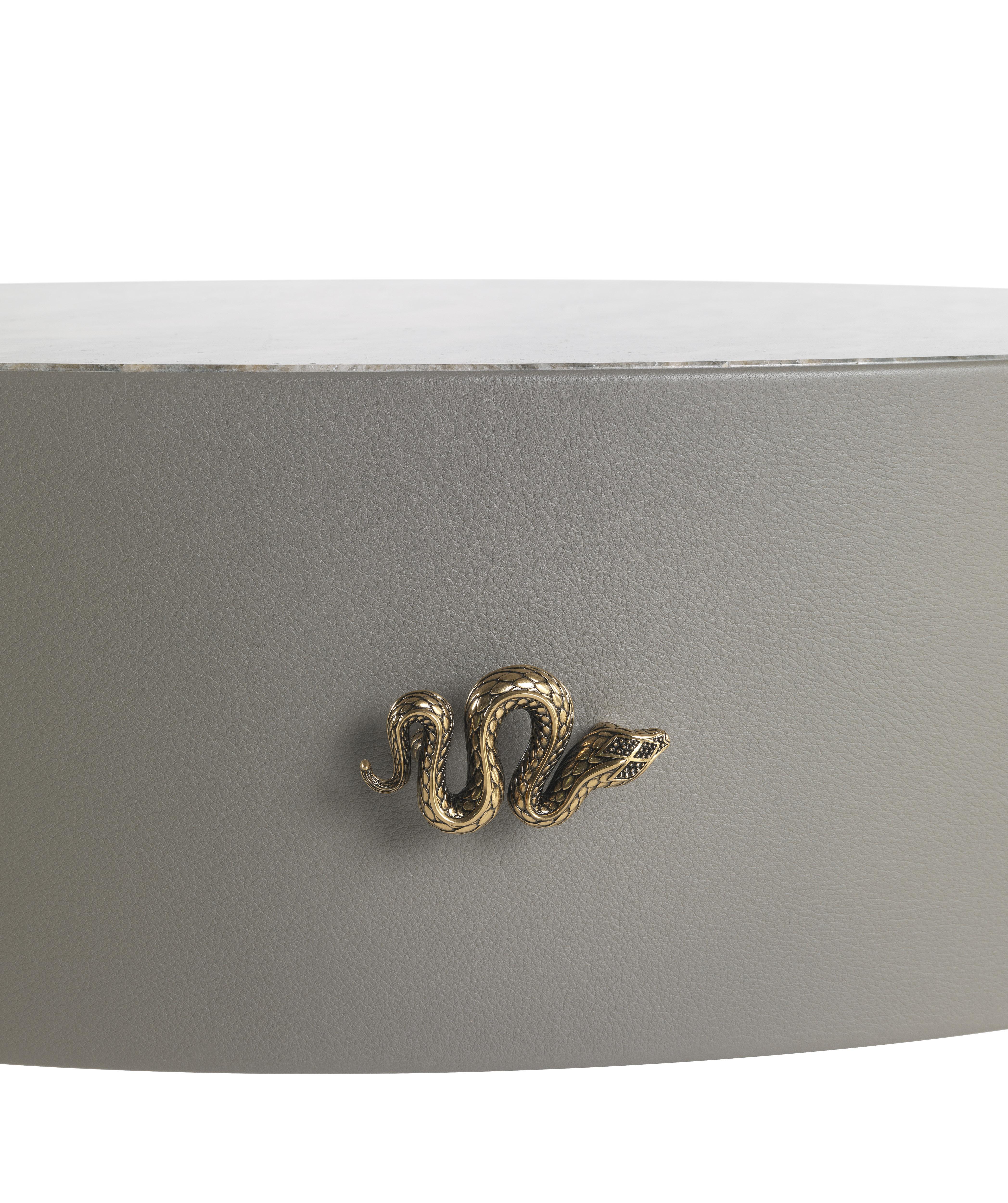 Trinidad Night table with structure in multi-layer wood covered with leather CAT. B touch COL. Ashgrey, top in marble CAT. A Bianco Carrara, legs in glossy gold finishing. “Jewel handles” and RC logo in cast brass available in gold finishing.