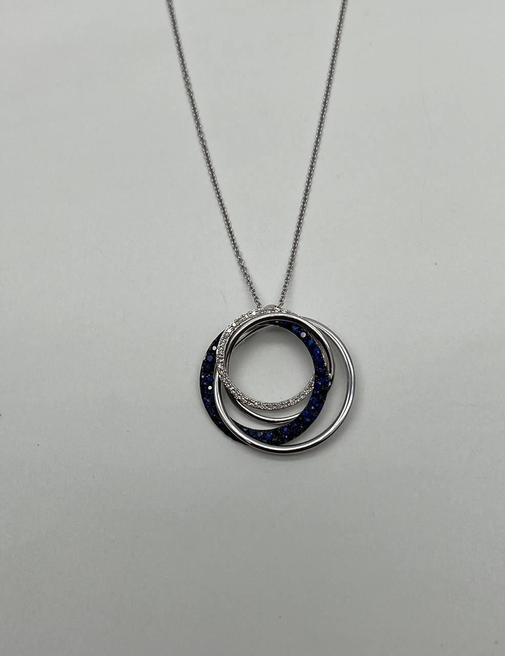 This elegant pendant necklace, features a captivating interlocking circle design. The pendant showcases a harmonious blend of shimmering blue sapphires and sparkling white accent diamonds, creating a striking visual contrast. The circles are