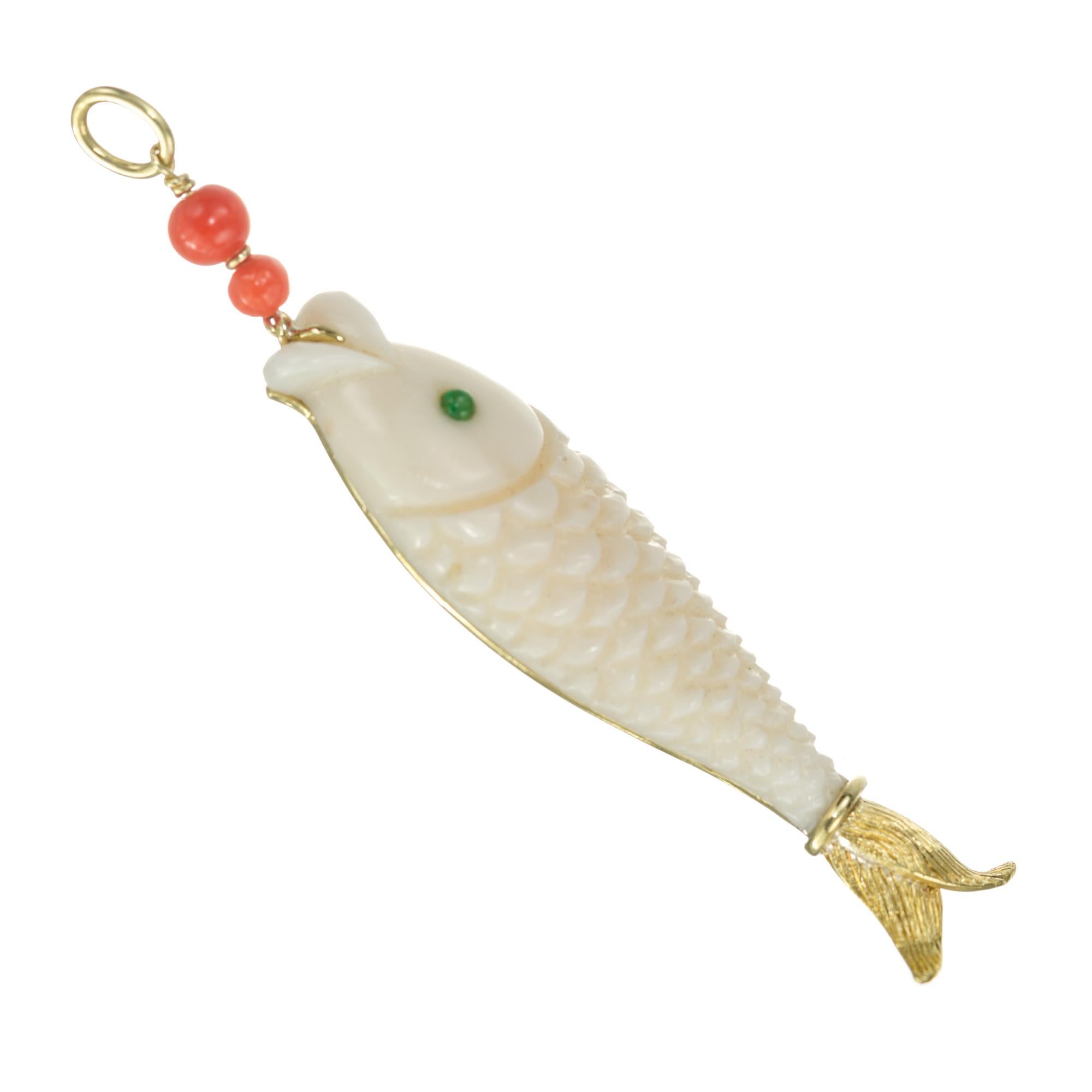 From the designer Trio. Vintage 1980's Angel skin coral fish pendant with an emerald eye and 3 orange red coral beads with a 18k yellow gold fishtail.

1 white carved coral fish
2 orange red coral beads
1 green cabochon emerald, approx. .5cts
18k