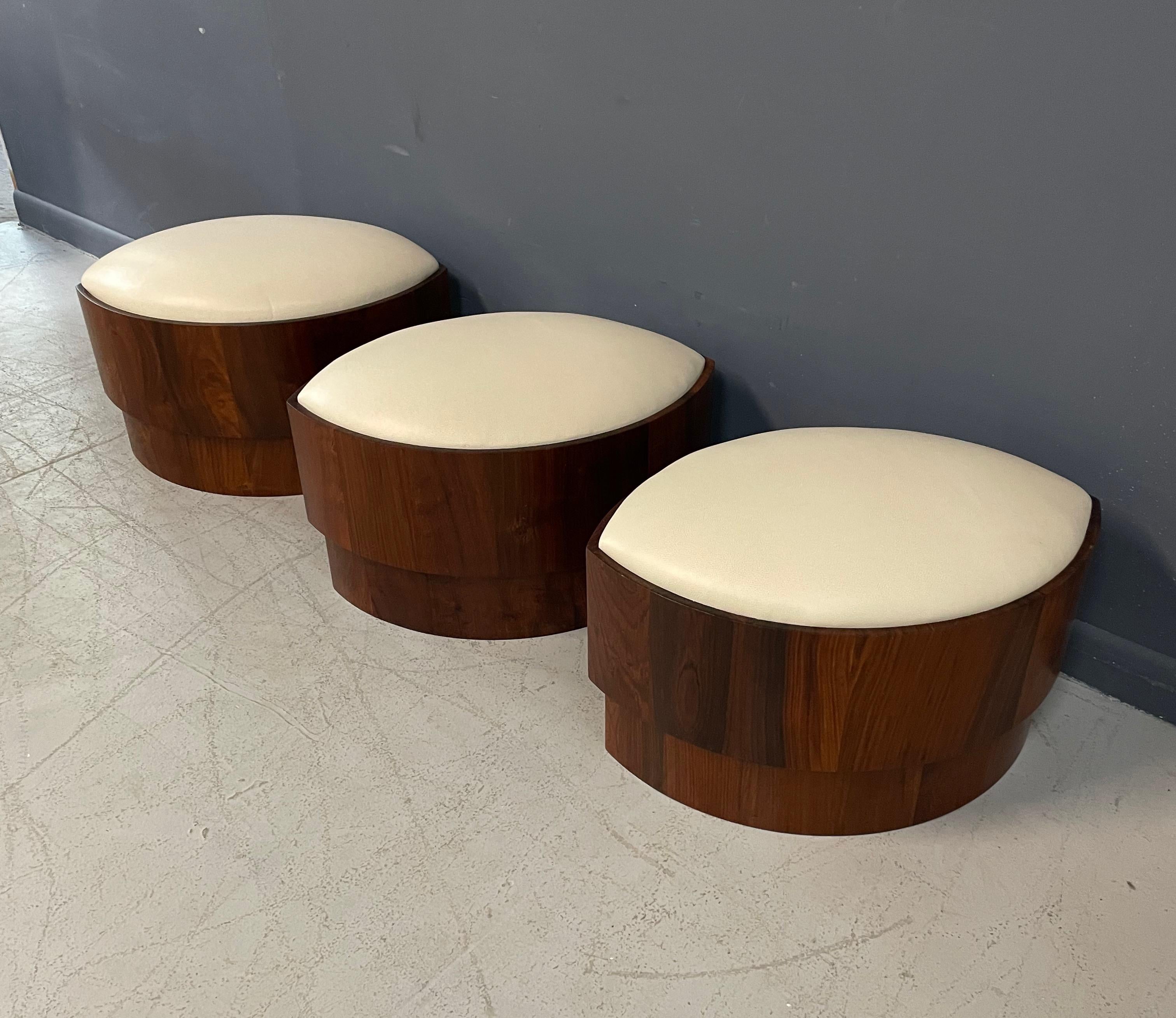 This set of leather topped ottomans or stools is constructed of beautifully grained wood with a padded top wrapped in soft buttery cream colored leather. The tops come off to reveal storage inside.