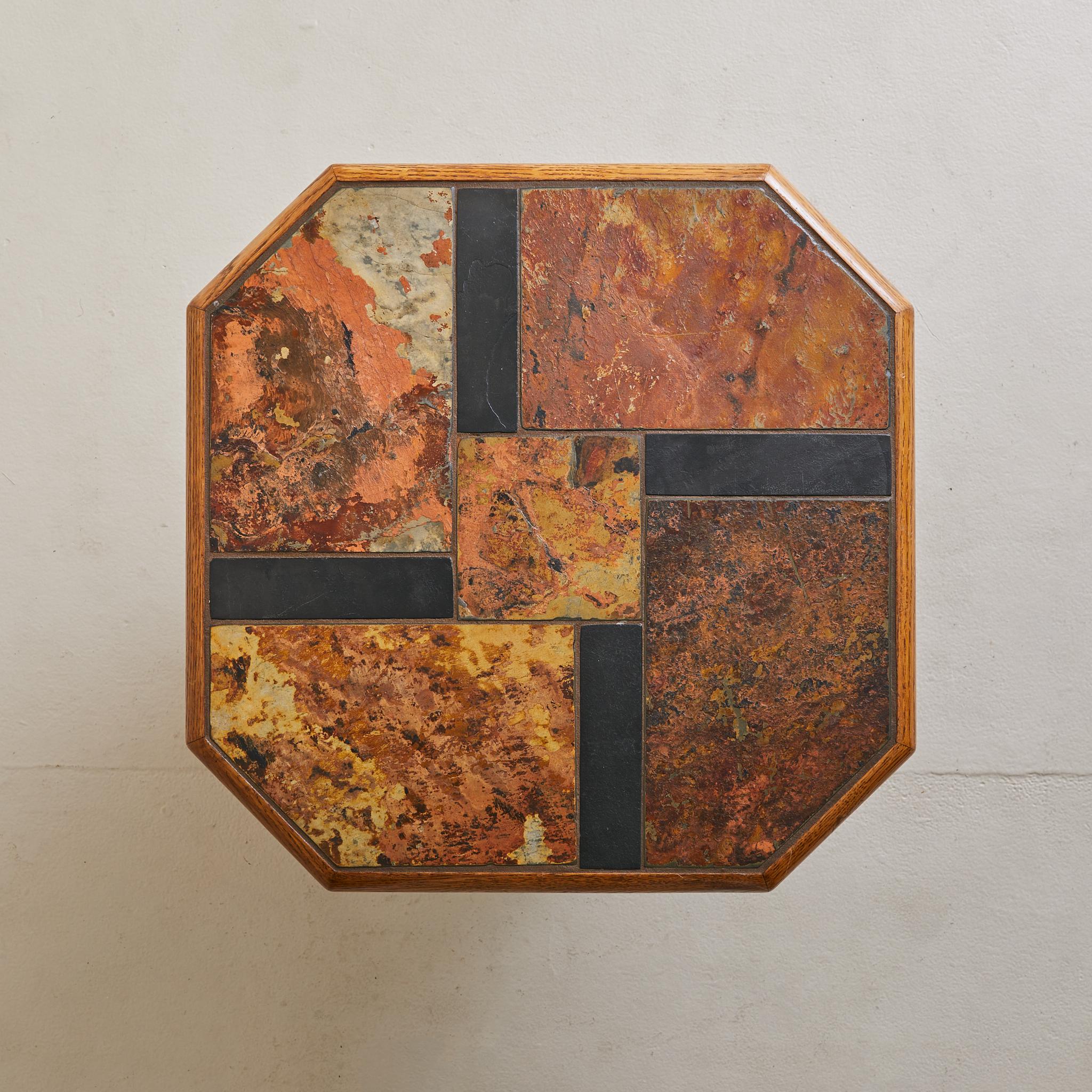 A sculptural trio of nesting tables, crafted in Belgium during the 1970s. Each features a faceted oak frame inset with a geometric patchwork of natural slate and stone, rich in rust, ochre, and charcoal tones. The octagonal tops are set at staggered