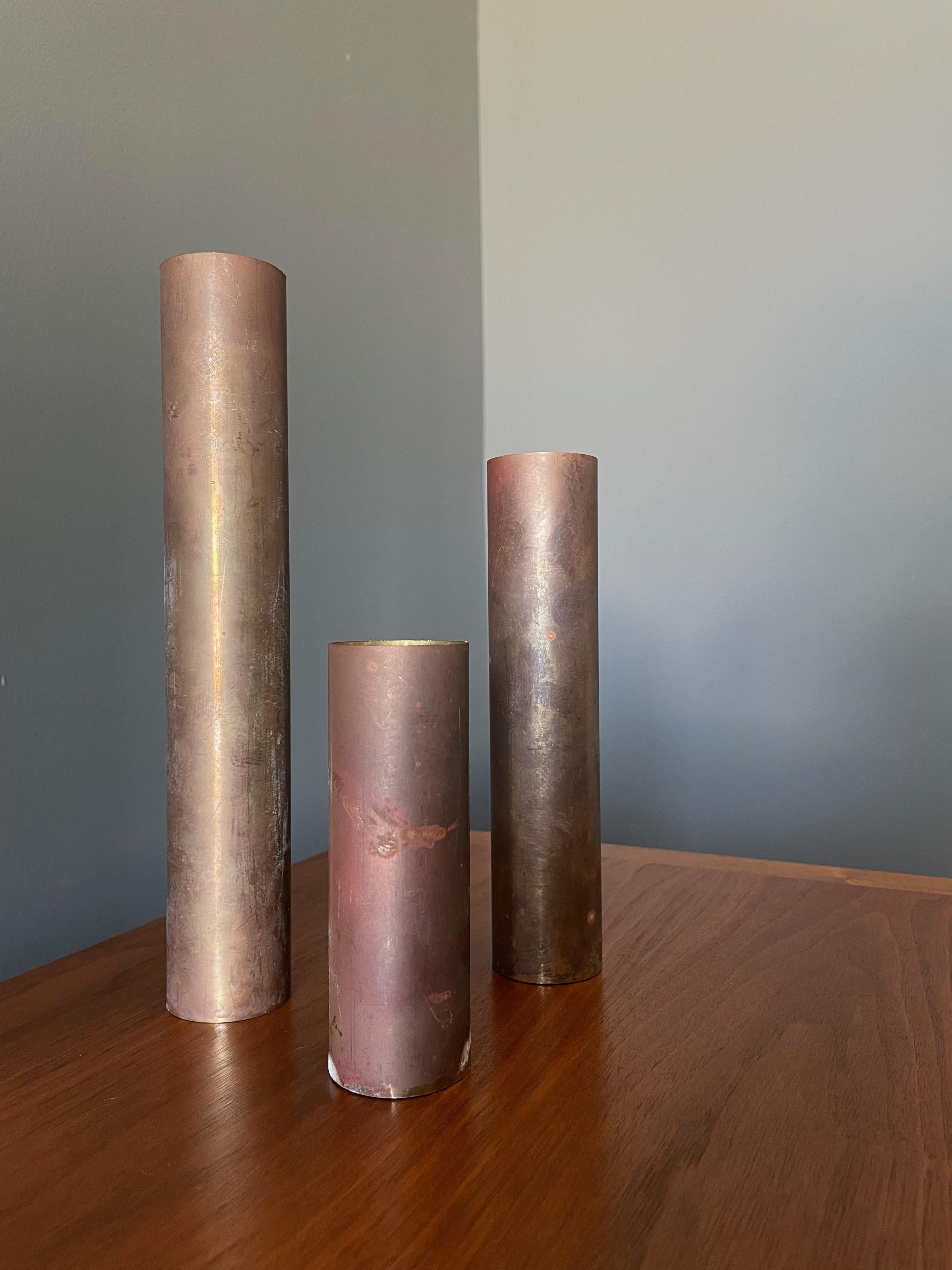 Trio of brass candle holders with heavy patina. Simple cylindrical design. Each holds a standard size votive candle. Graduating in size from 9.75