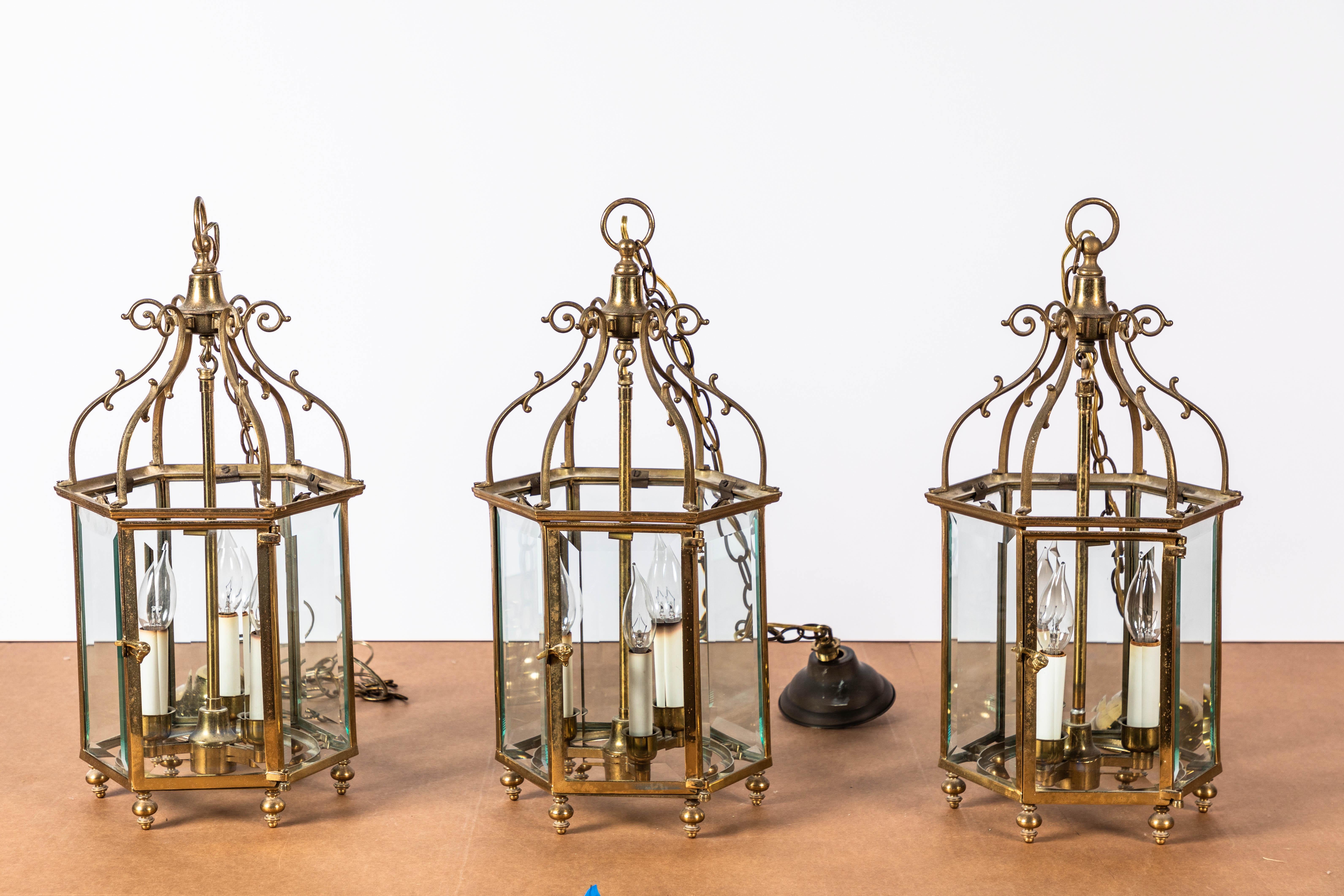 Set of three 20th century English handcrafted brass Georgian style lanterns with beveled glass. Each lantern has three candle lights. Various chain lengths of 20