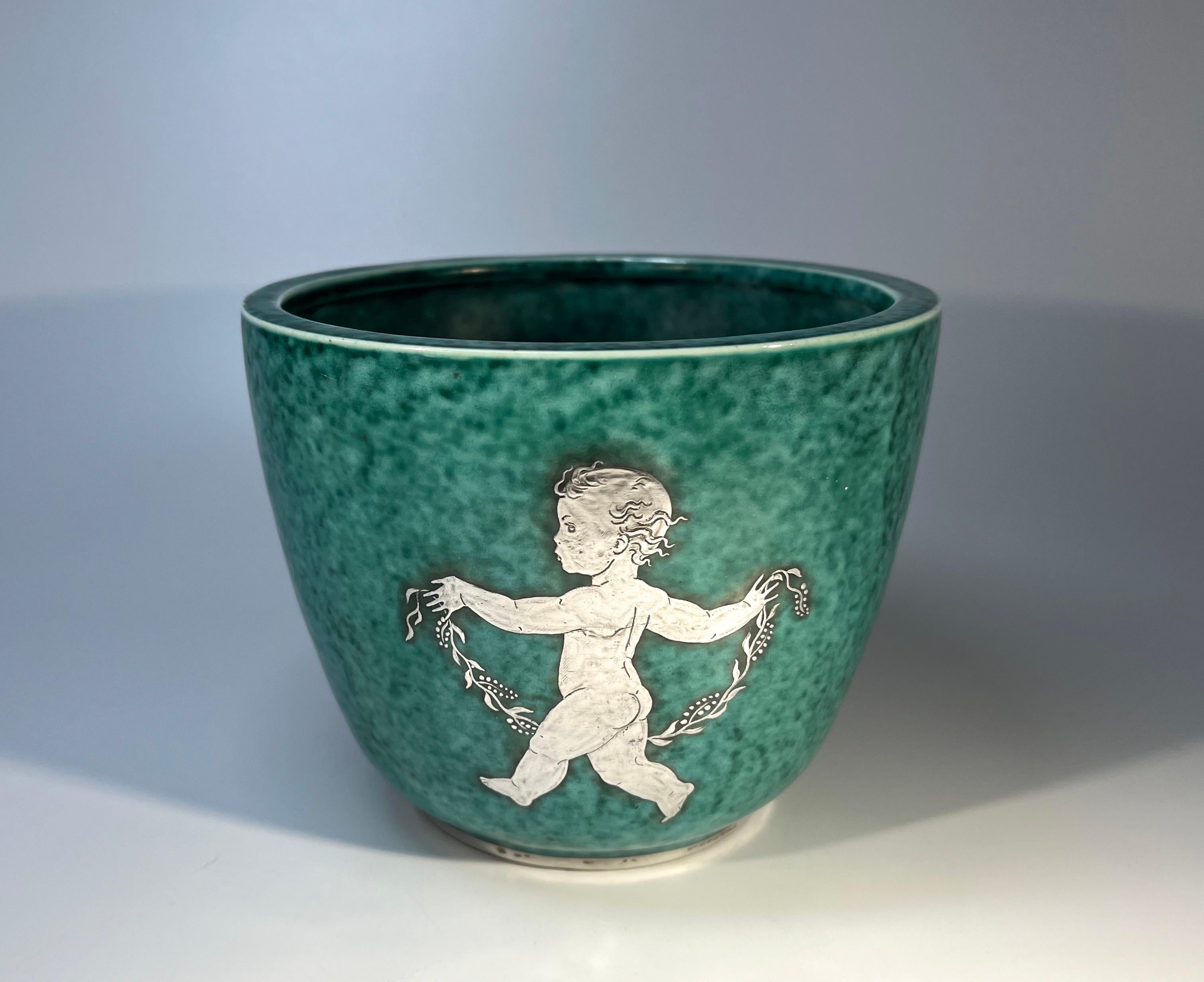 A trio of cherubs with garlands decorate this cache pot designed by Wilhelm Kage for Gustavsberg, Sweden.
Argenta stoneware piece, characterised by the mottled green glaze and applied silver decoration
Circa 1937. Date letter G
Signed Gustavsberg I