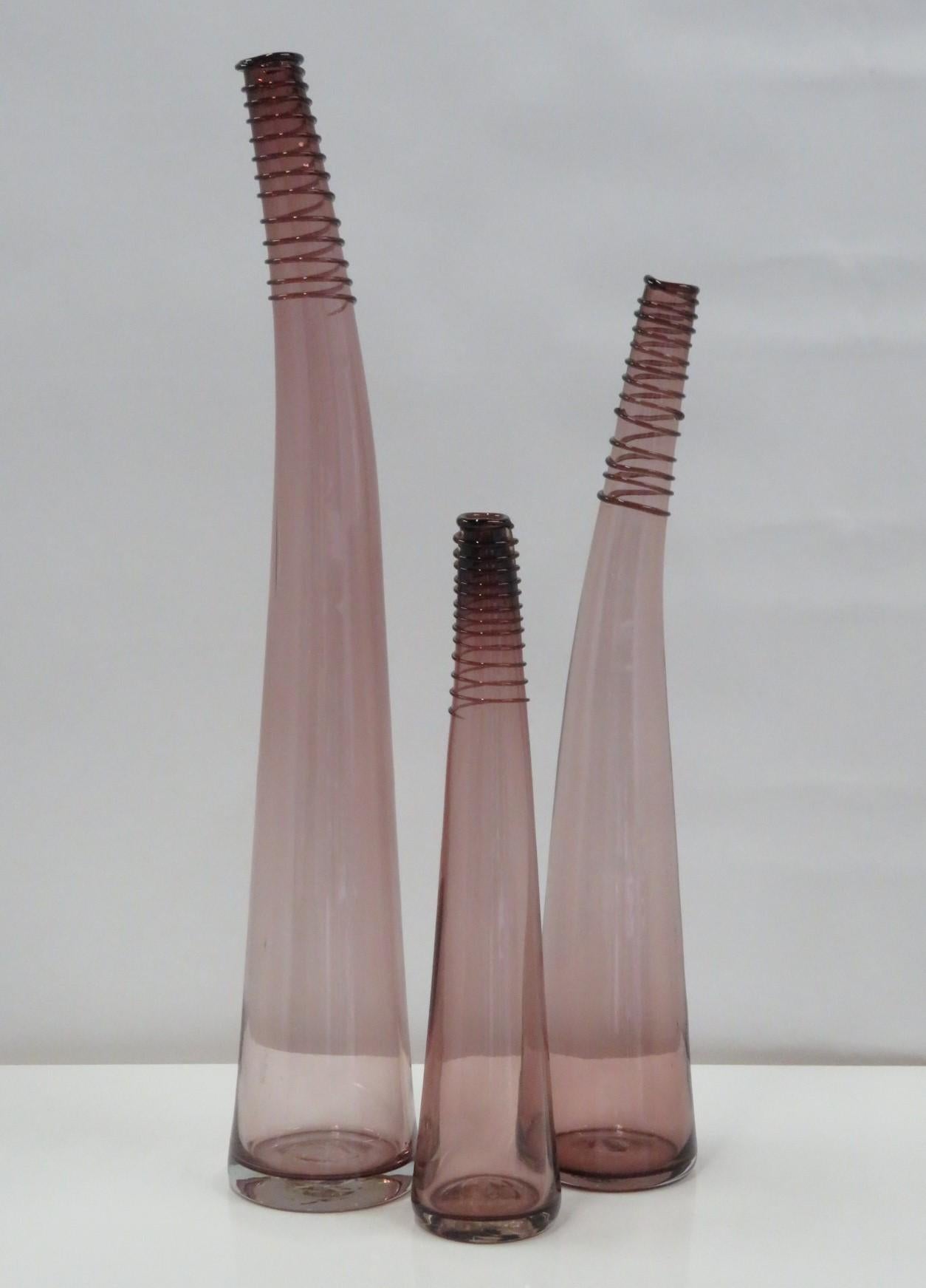 Blenko Set of 3 of Bent Spiral Neck Bottle Vases, in three heights, created by Don Shepherd in 1988. This designed makes its debut in the 1988 Blenko catalog and assigned number 8827 l/m/s depending on the height of the vessel. Beautiful purple