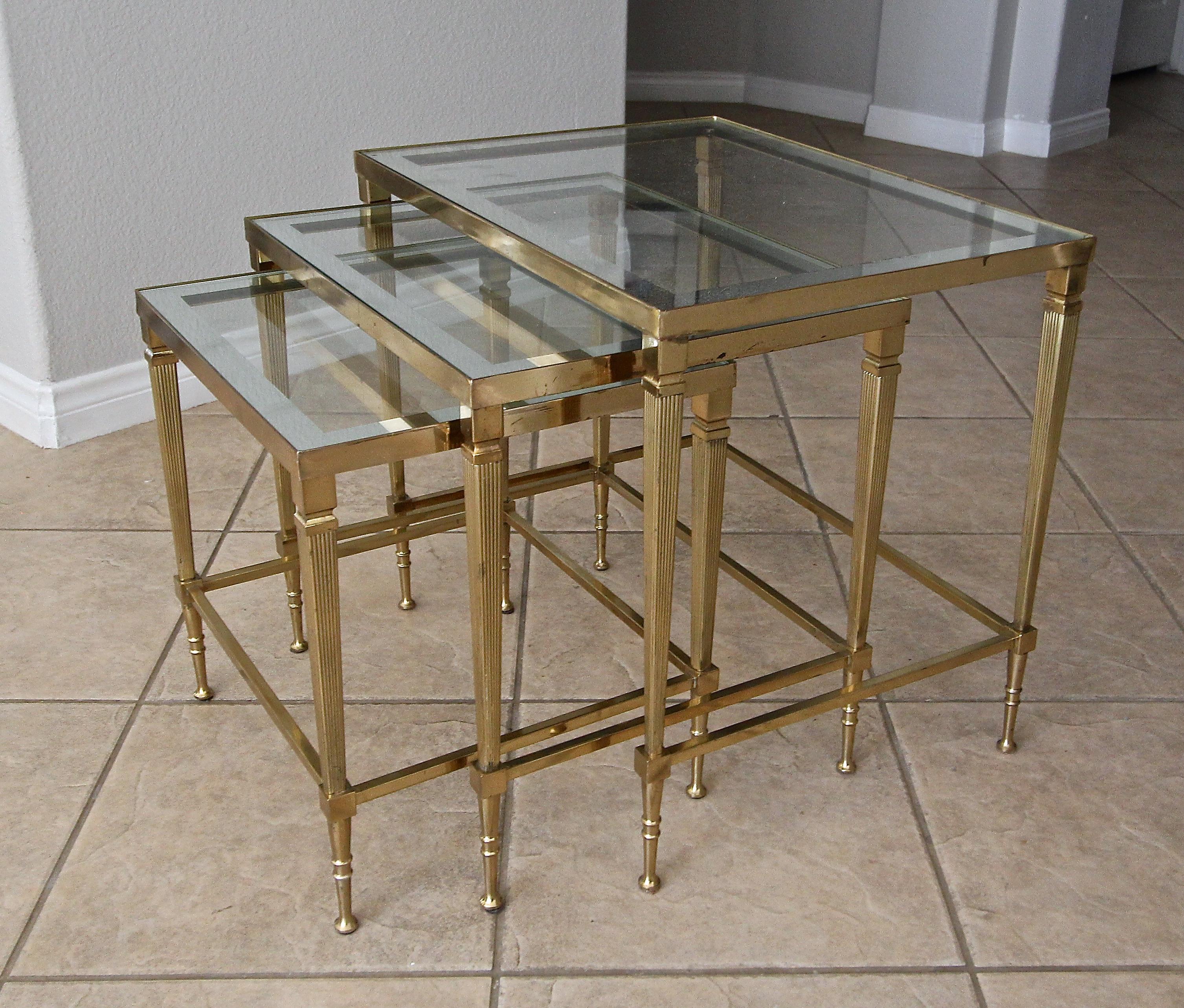 Trio of Maison Jansen brass nesting tables with mirrored edge glass tops. Nice original finish with age appropriate oxidation spots. Two of the glass tops are newer replacements, the larger one is original with some oxidation mirror loss. See photos