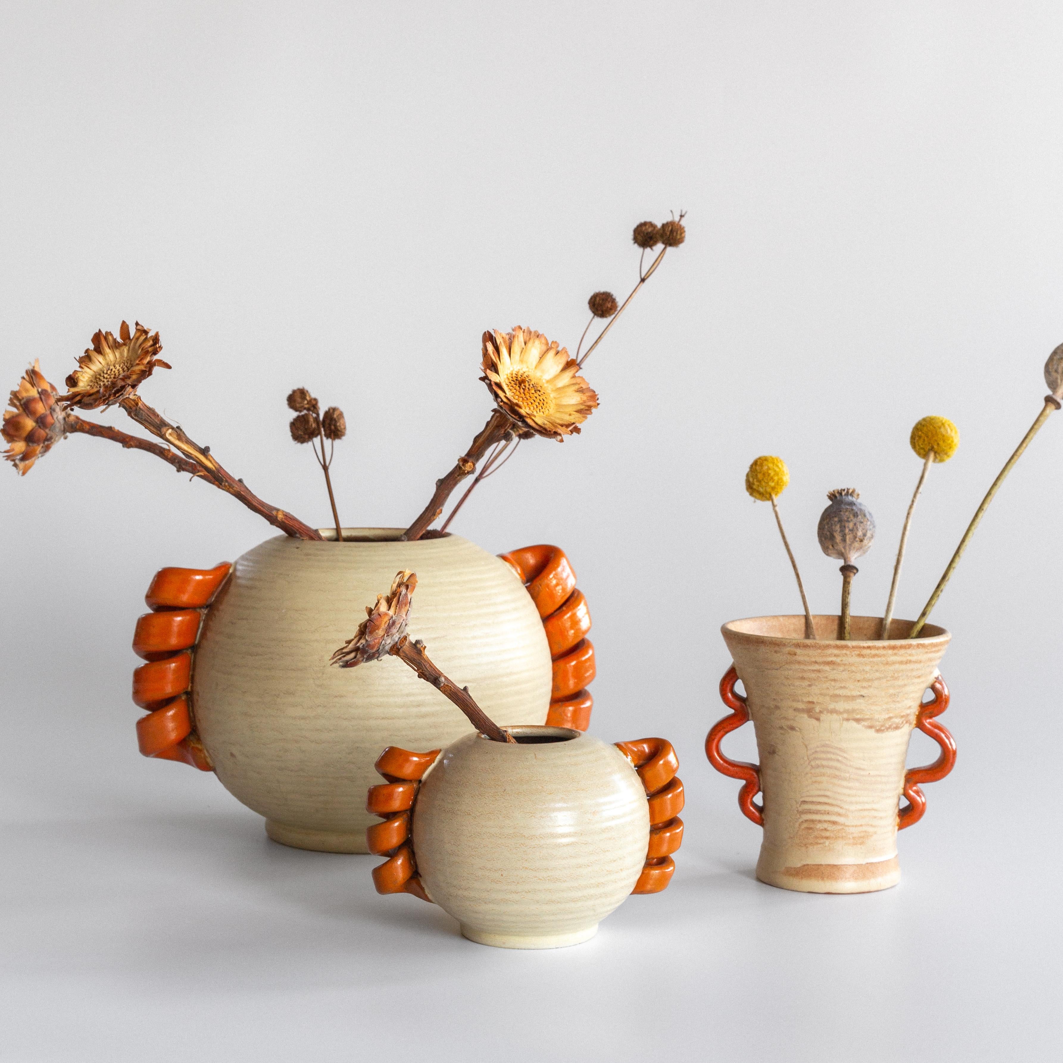 Un raro set di tre vasi in ceramica modernista provenienti dalla Svezia, ognuno dei quali è caratterizzato da manici ornamentali. Prodotti negli anni '30 da Andersson & Johansson di Höganäs, questi vasi di terracotta sono smaltati in un beige