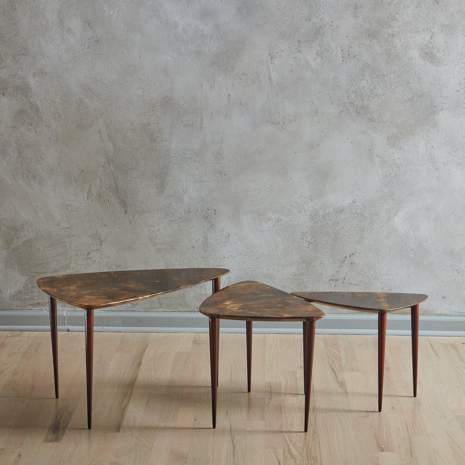 A trio of 1950s Italian side or coffee tables in the style of Aldo Tura. These tables feature triangular tabletops with rounded edges and have a lacquered parchment finish in a deep brown hue with subtle color variations. They stand on tapered