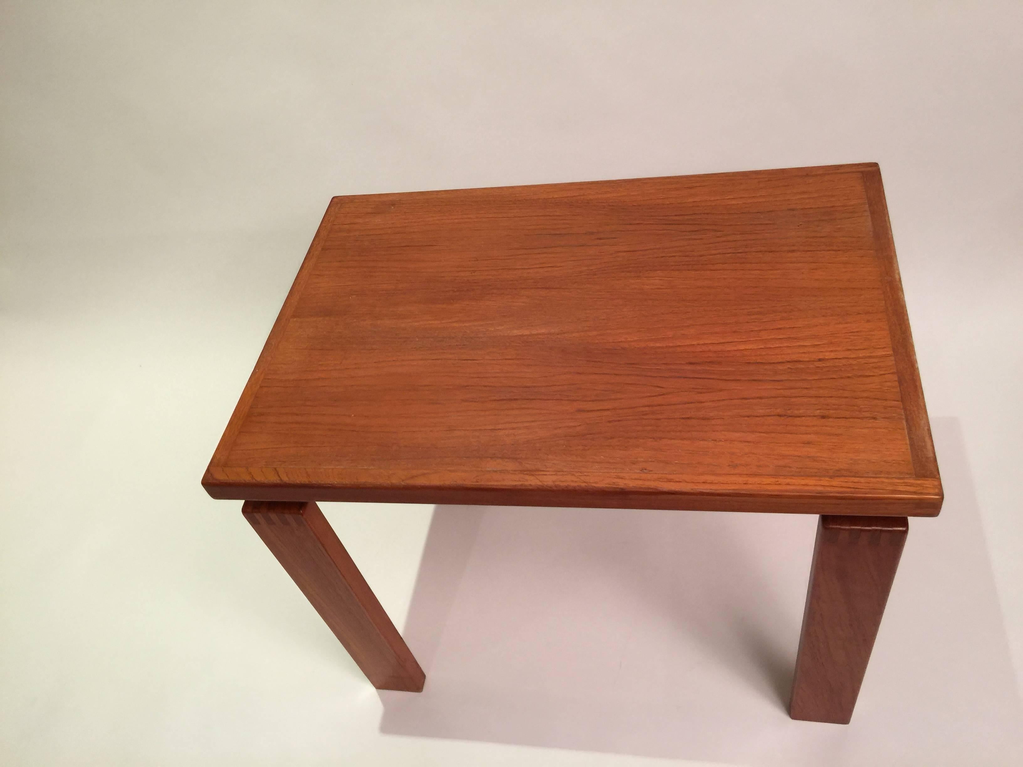 Solidly built and simply designed this teak side table features a floating top with dovetailed accents on the corners of the table top and legs. This late modern design is robust and practical with a design to suit any space.