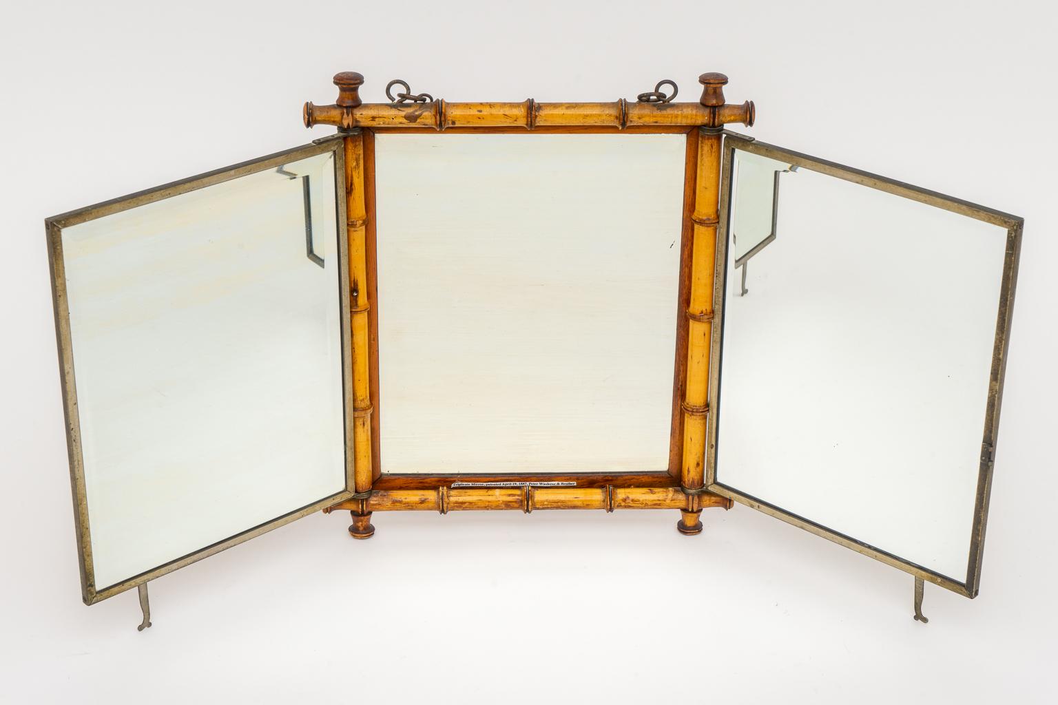 This stylish and chic Aesthetic period faux (wood) bamboo trifold beveled mirror dates to 1887 and was created by Peter Wiederer & Brothers. The piece can be hung on the wall or could sit on a vanity or shaving table. The backside is detailed with