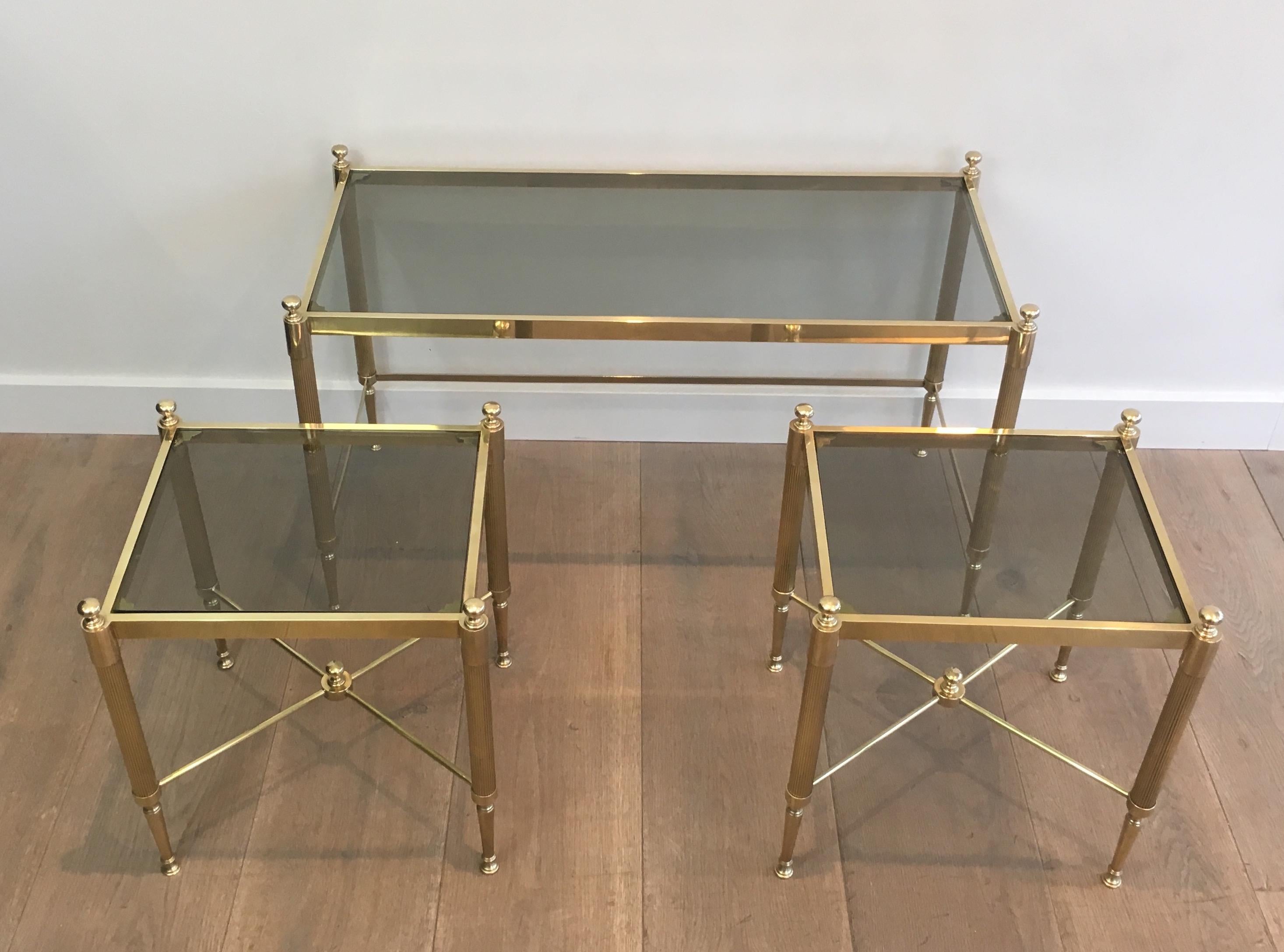 This very nice tripartite coffee table is made of brass with greenisg glass shelves. The table is made of a main table and 2 nesting side tables sliding under the main table. This is a French work, circa 1970.