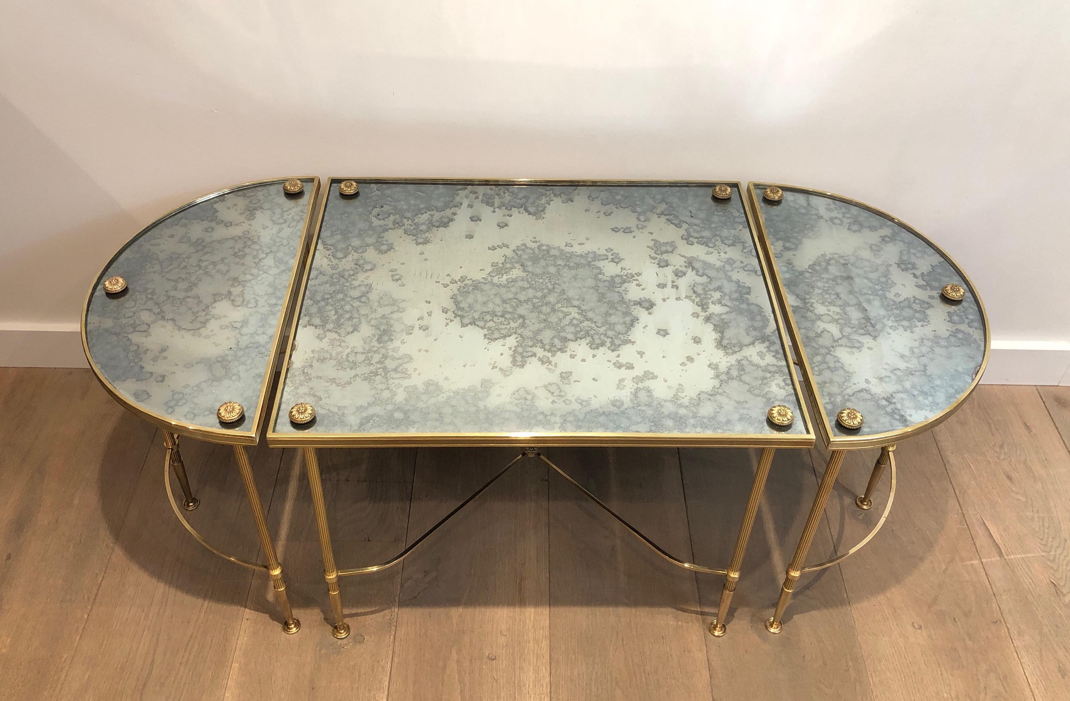 This tripartite coffee table is made of a main rectangular table and 2 matching rounded side tables. This cocktail table is all made of brass with original eglomized mirror top. This is a work by famous French Designer Maison Baguès.