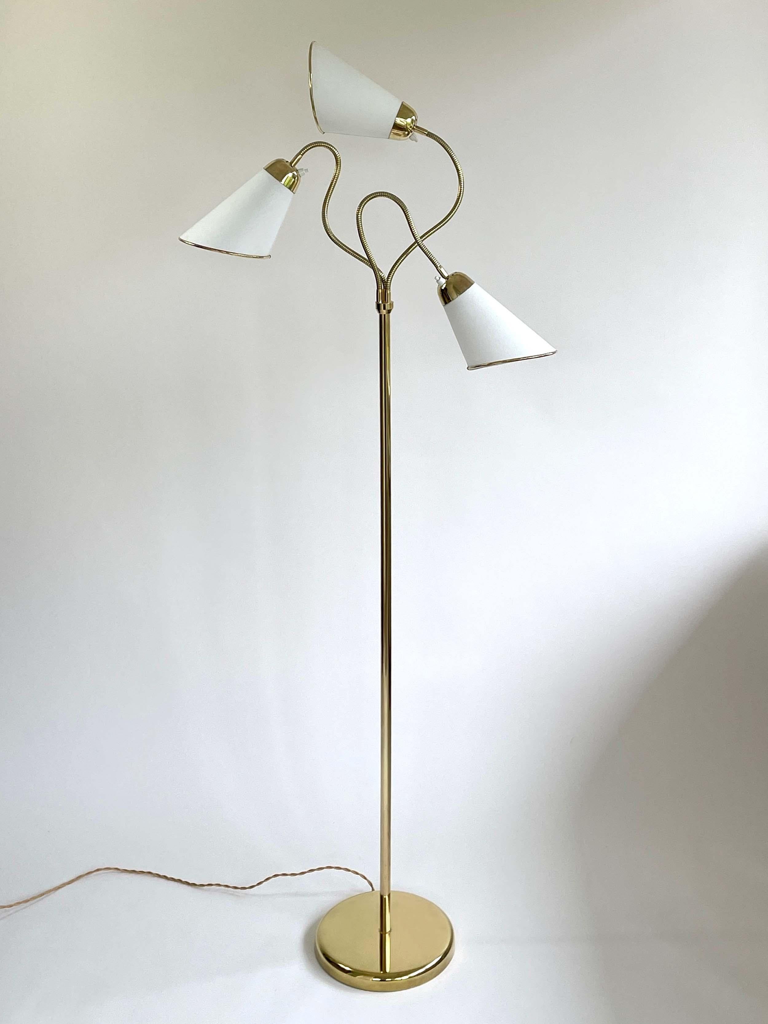 This unusual midcentury brass gooseneck floor lamp was designed and manufactured in Sweden in the 1950s.

The lamp features a round brass base and three adjustable gooseneck lamp arms with off white cotton lampshades. The fabric shades have been