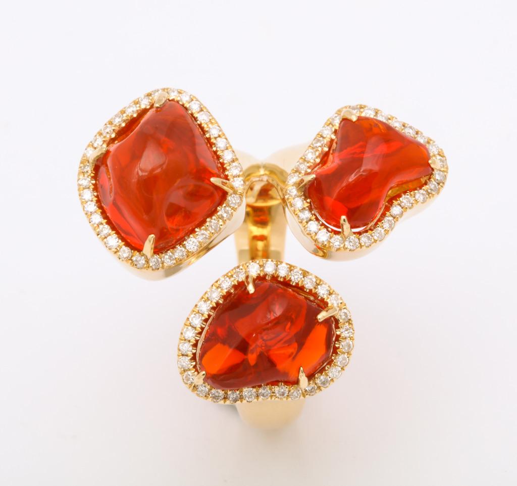 The triple stone ring is comprised of three baroque, free-form cut Mexican fire opals (3=7.21cts) each encircled with diamonds (0.36cts) and set in 18kt yellow gold.  A one of a kind, bright vivid orange show stopper.  Size 6 1/2

Fire opals