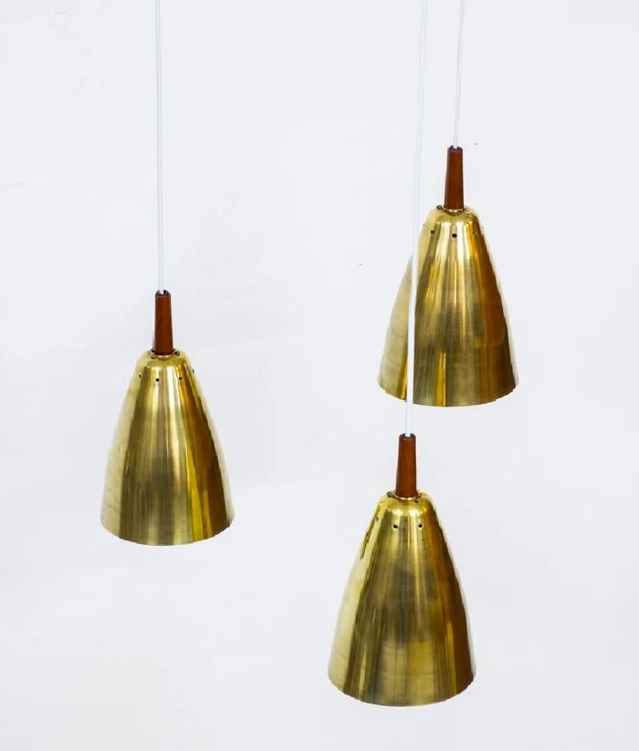 Magnifica lampada a sospensione regolabile in altezza con triplo paralume in ottone massiccio e teak, progettata da Hans Agne Jakobsson e prodotta dalla sua azienda ad Åhus negli anni '50. Il triangolo in teak massiccio porta la firma del designer.