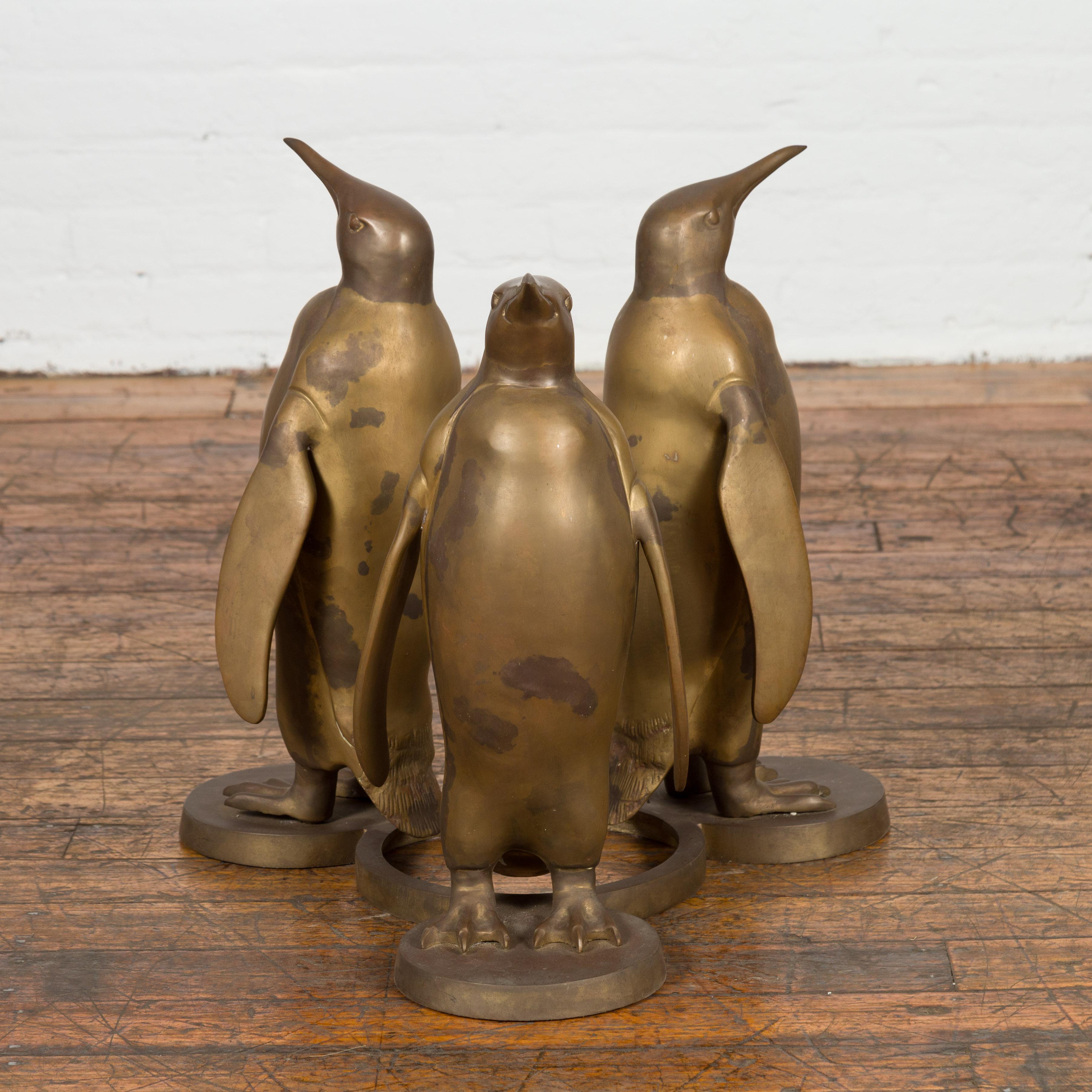 A bronze animal sculpted ground depicting three penguins depicted back to back, in gold patina. This vintage bronze sculpture captivates with its masterful portrayal of three penguins, meticulously sculpted back-to-back in a unified stance. The