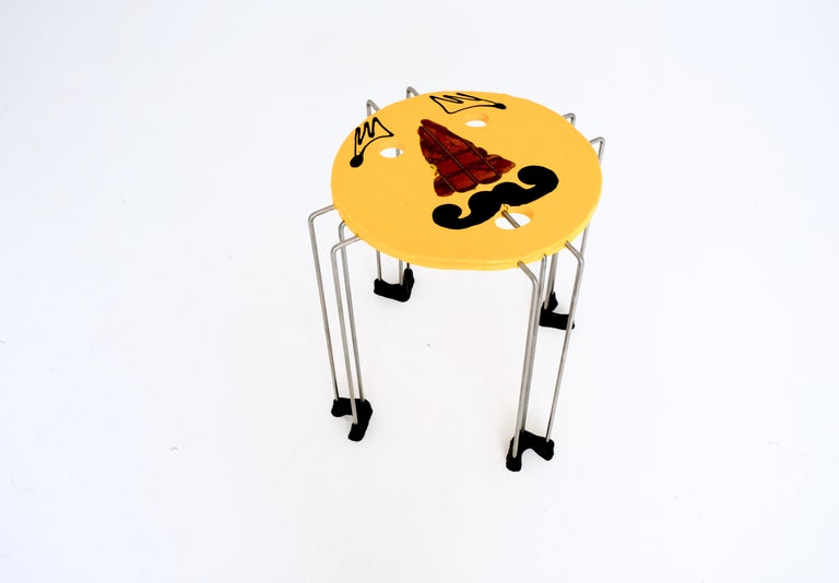 In 1995 Gaetano Pesce designed the “triple play” series of resin tables. the table shows a cartoonish face with moustache on a yellow background, also on steel rod legs, here with black feet (stamped underneath with manufacturer’s mark “fish design