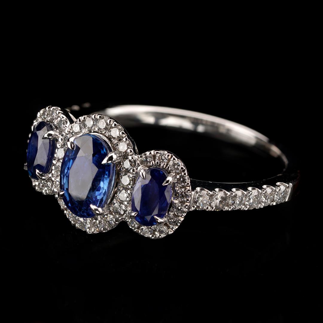 This stunning past present future three-sapphire statement ring features one large 0.95 carat oval-cut deep Ceylon blue eye-clean sapphire set centrally and surrounded by a single halo of sparkling, contrasting round white diamonds. Flanking the