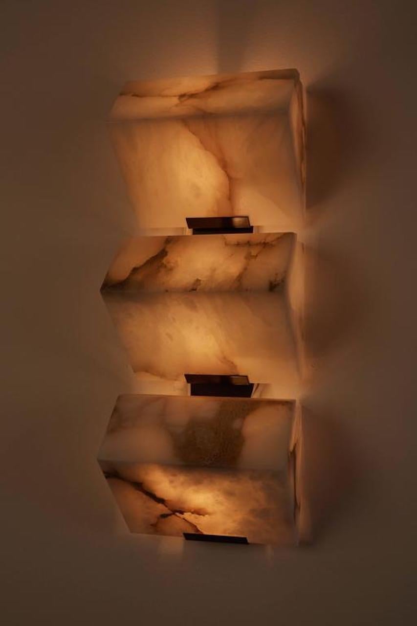 Originally designed in 1923 this current production by Galerie MCDE of France of the triple sloping wall lamp by Pierre Chareau is composed of three blocks of alabaster mounted on an enameled stainless steel frame. This wall lamp is also available
