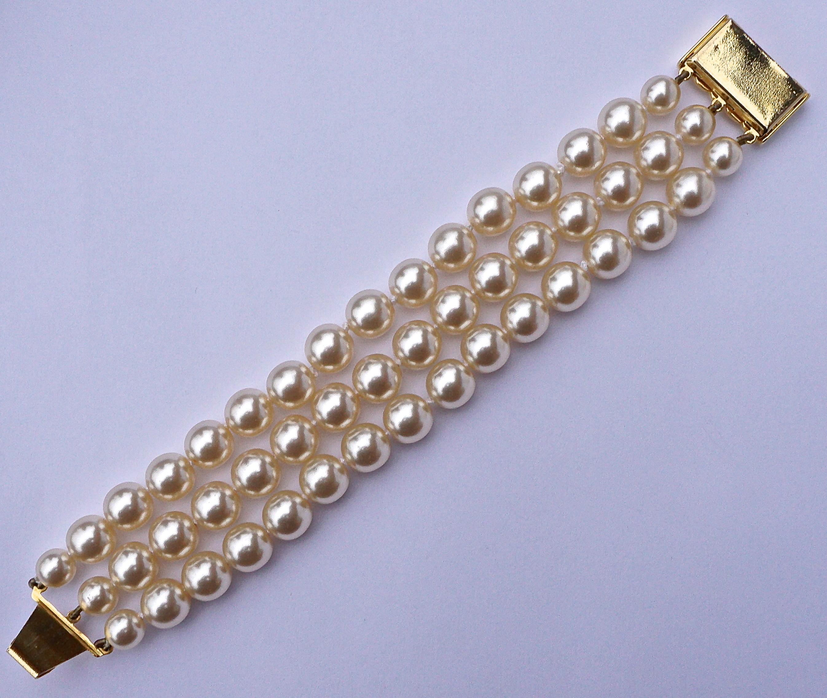 Three strand faux pearl bracelet featuring a lovely fancy gold tone clasp with a diagonal ridged design. Circa 1970s. There are knots separating each pearl. Measuring length 18.8cm / 7.4 inches, by width 2.9cm / 1.14 inches. The bracelet is in very