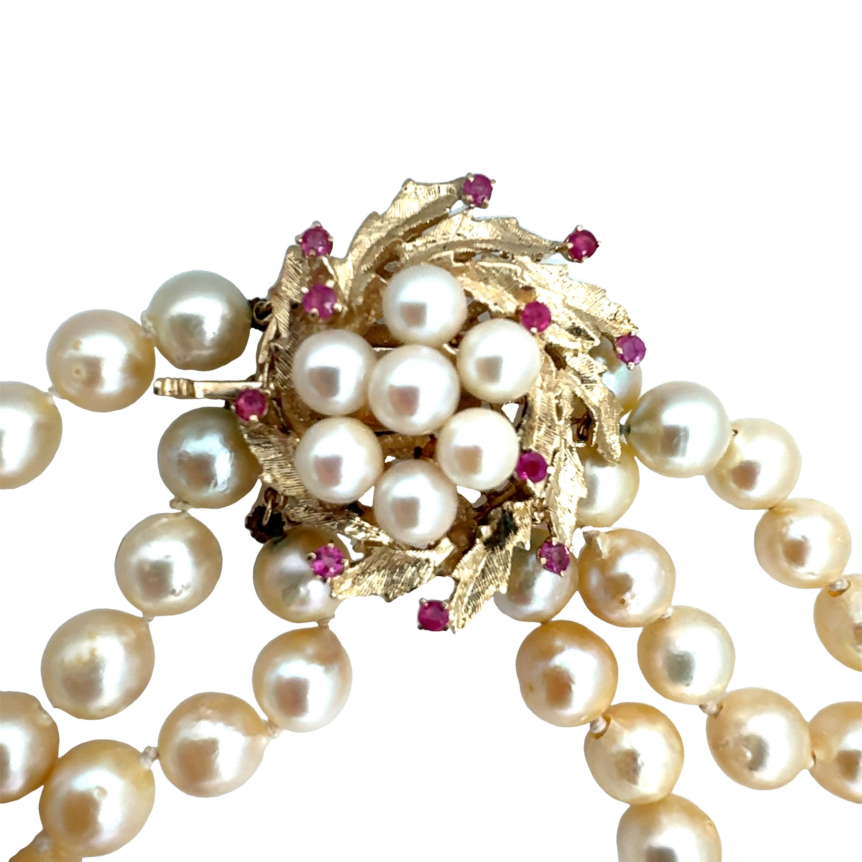 One triple-strand pearl necklace featuring 140 round, cream color cultured pearls measuring 8.00 millimeters in diameter on average. 14K yellow gold Florentine finish clasp with 11 prong set, round brilliant cut rubies weighing 0.44 ct. in
