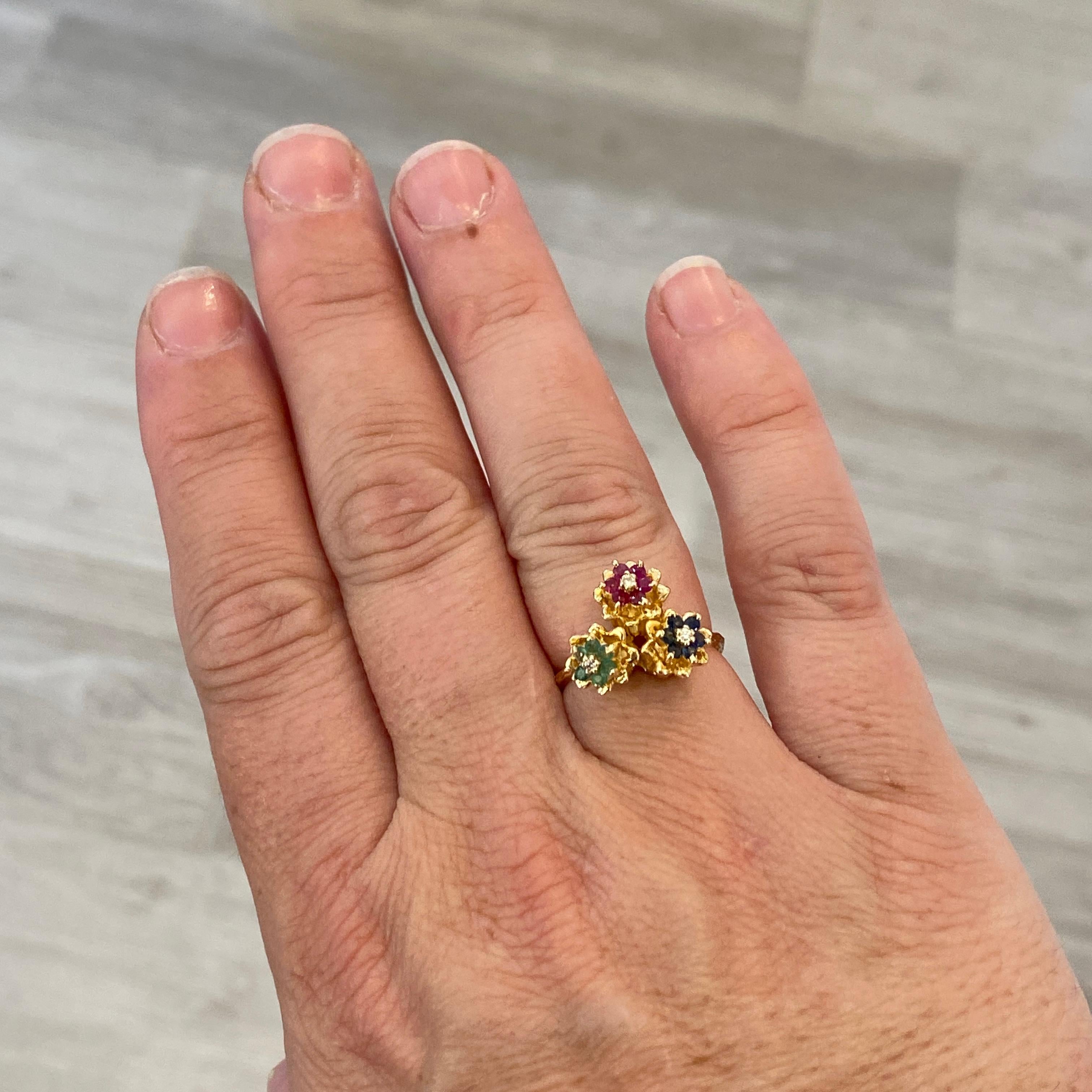 Dieser schöne Tulpenring hat drei Edelsteinblüten, die mit den drei großen Edelsteinen besetzt sind: Saphire, Rubine und Smaragde. Jede Blüte ist in der Mitte mit einem Diamanten besetzt. Tulpenringe waren in den 1970er und 1980er Jahren sehr