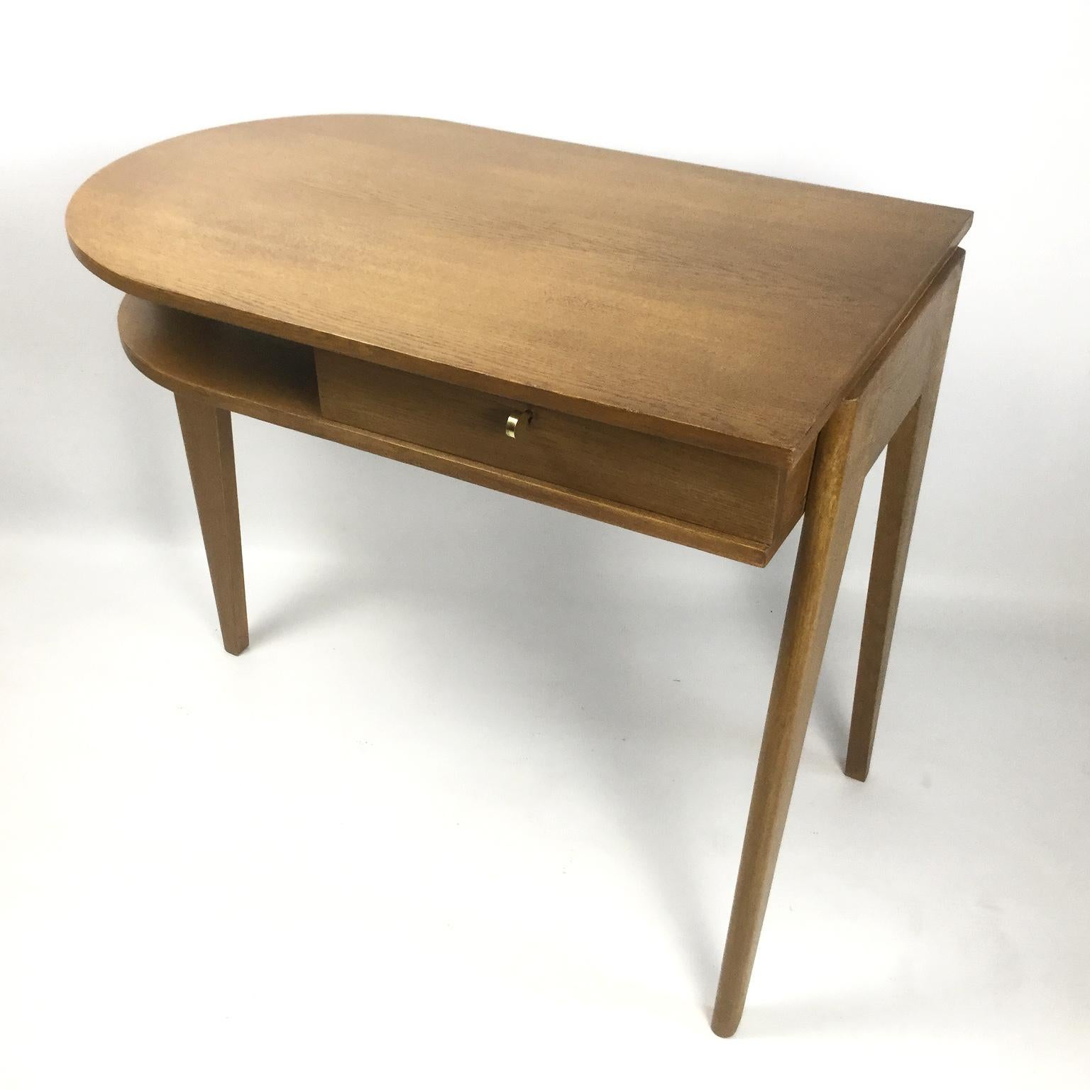 Oak desk with the rectangular top rounded to the right. 
Opens on the front with a drawer and an open niche 
The lock and key are in good working condition
Tripod base with a flat post slightly protruding from the top.
Postmodernism Movement