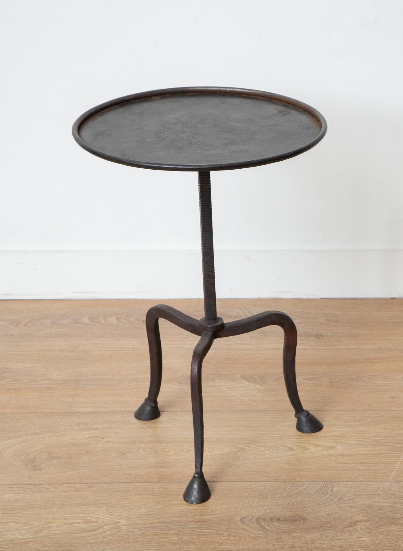 Tripod hand-forged side or drinks tables, in stock.
This stunning wrought iron tripod side table with hoof legs is an eye-catching addition to any home decor. Its round top features a lip, and its hammered metal frame has a beautiful black patina