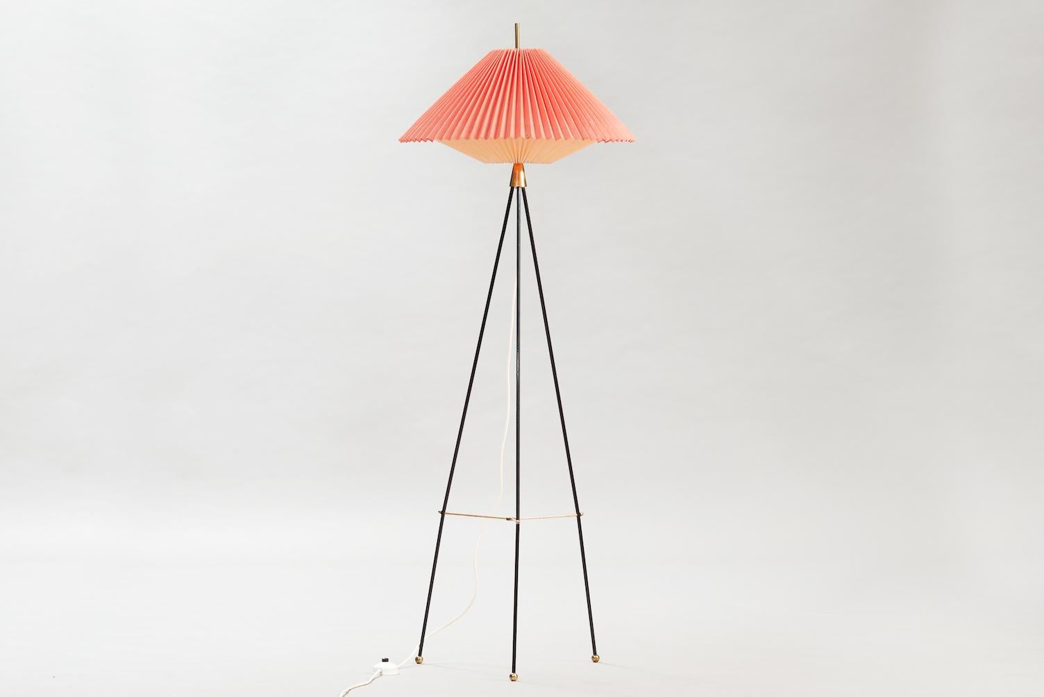 Midcentury tripod black lacquered metal and brass floor lamp with a white and red pleated paper shade.