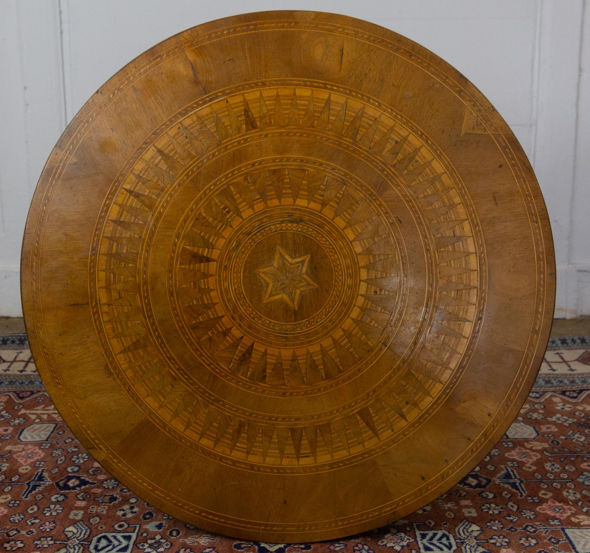 This elegant Italian gueridon from the 19th century is made in walnut and has a very beautiful inlaid top with star decorations, surrounded by two inlaid belts forming suns, finished on its edge with a net.. Its alternating walnut and mahogany base