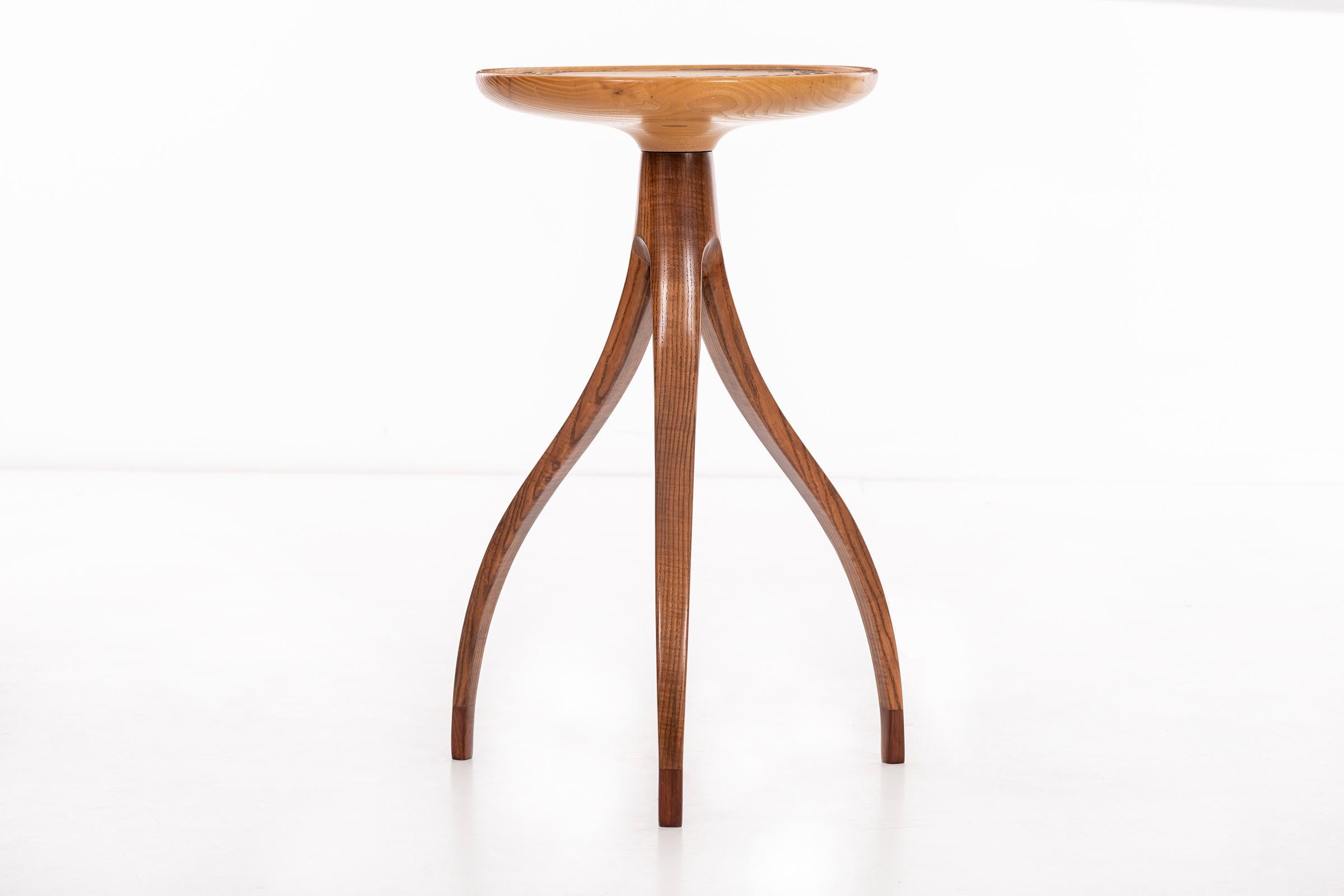 Slender scale high tripod table, solid carved bleached walnut lip edge top with ceramic design detail inset.
Feet have darker tone wood accent.
