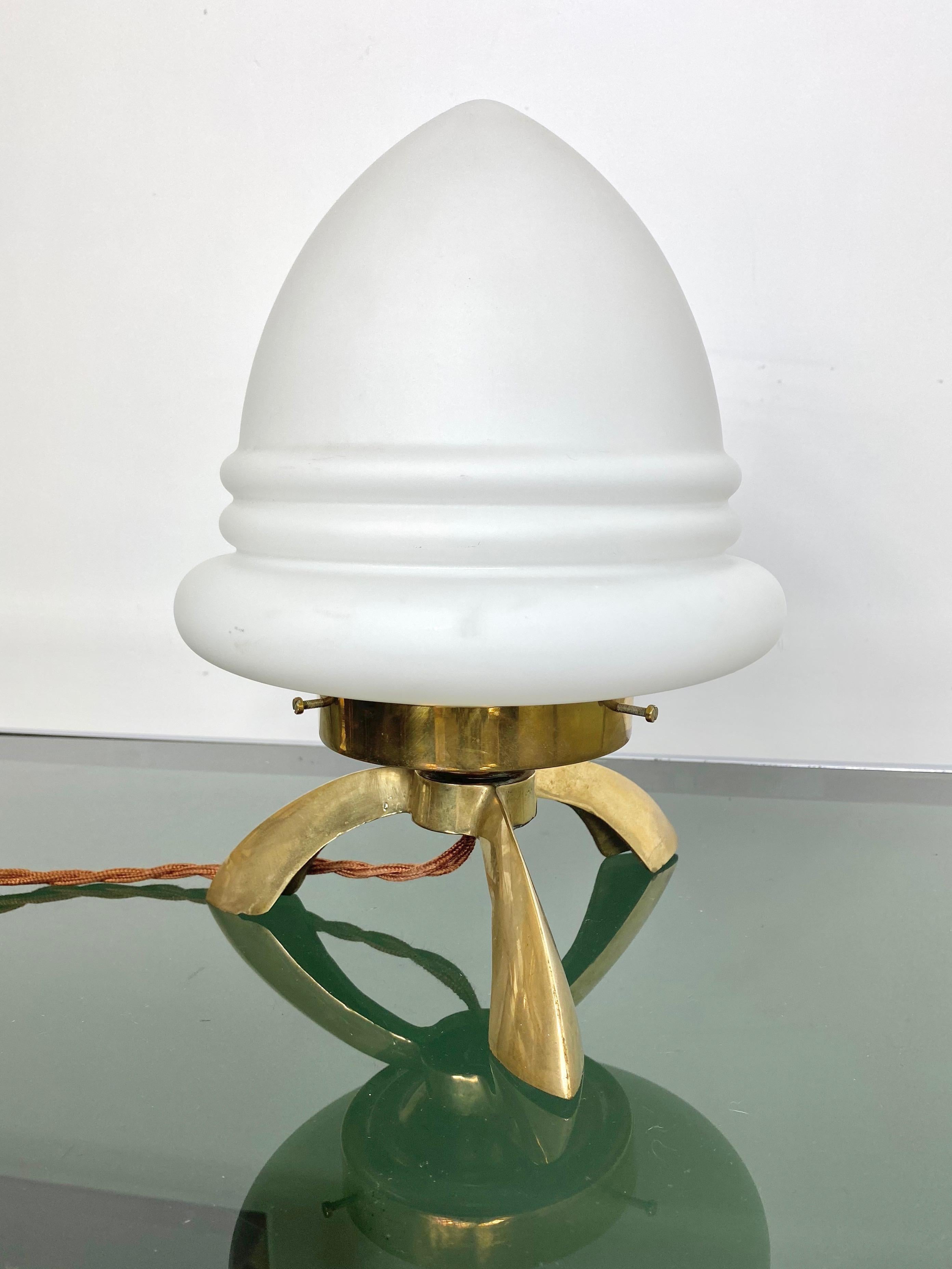 1960s table lamp in a brass tripod base executed in sculpturally blown opaline glass in the shape of an rocket shuttle. The unique style is highly suggestive of the Italian designer Angelo Lelli for Arredoluce.