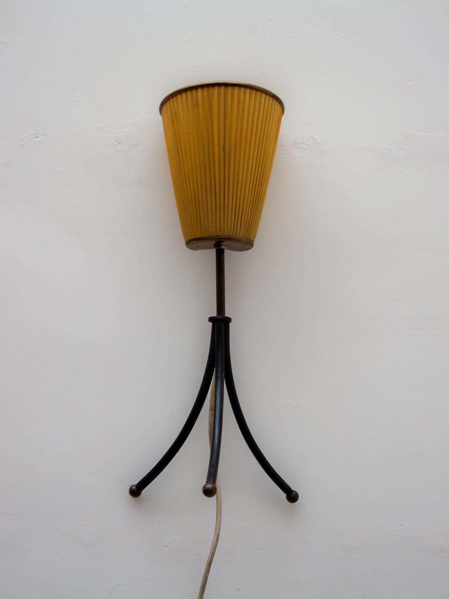 Cette lampe de table ou de chevet des années 1950 est dotée d'un trépied en métal laqué noir et peut être accrochée au mur en tant qu'applique. La lampe est dotée de l'abat-jour d'origine en soie fine pour une lumière chaude et magnifique. La pièce
