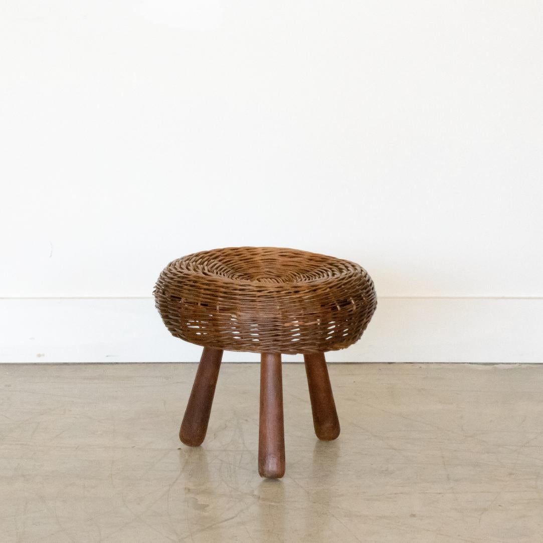 1950's circular wicker stool with three dark wood legs by Tony Paul. All original with some small pieces of wicker missing.