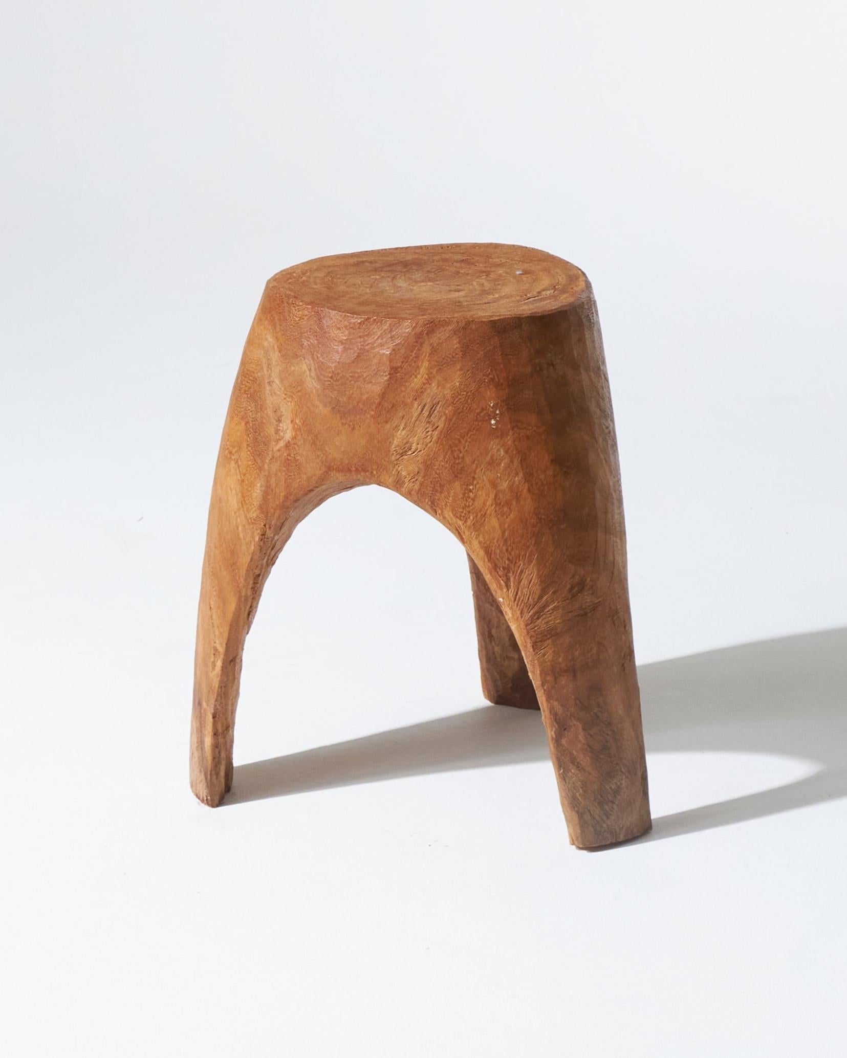 Dreibeiniger Hocker aus rohem Holz. Ein handwerklich hergestellter Sitz mit einfachen, robusten Linien, direkt aus einem massiven Stück Holz geschnitzt.