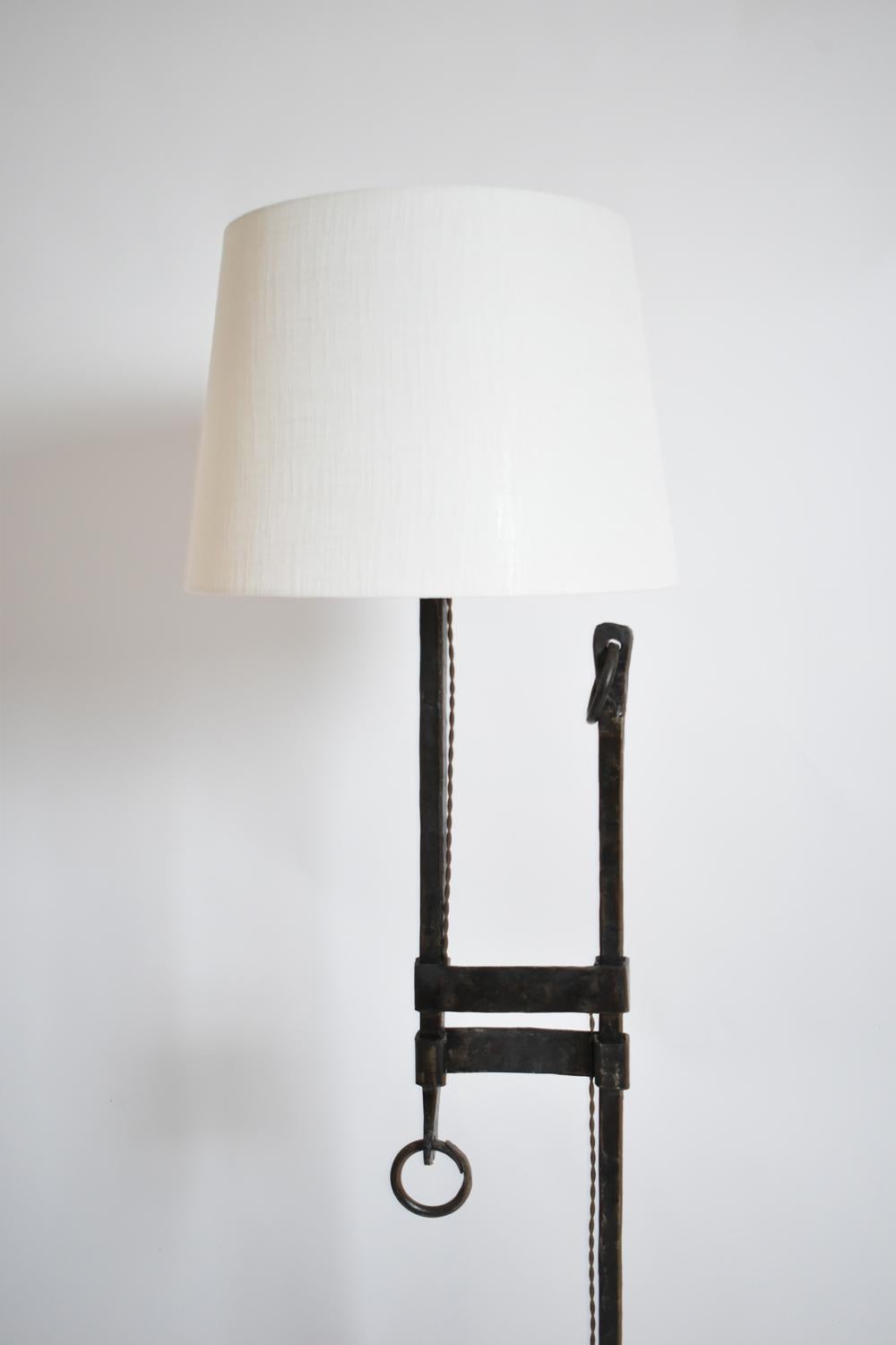 Floor lamp in wrought iron with a black patina, resting on a tripod base, decorated with rings. France, 1950s.