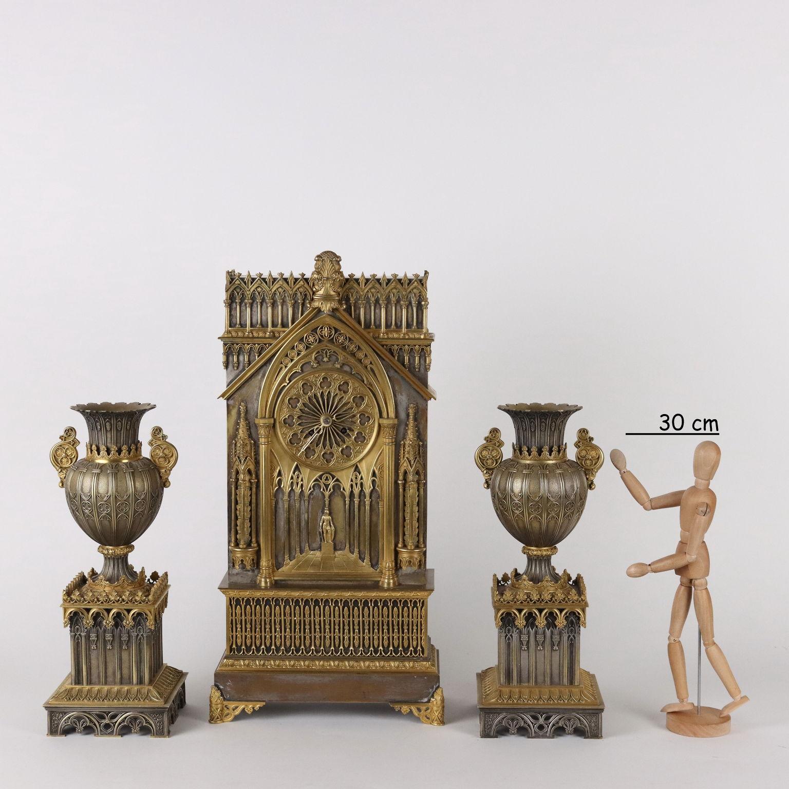 Neo-Gothic clock triptych in gilt bronze. The front of the clock reproduces the facade of a neo-Gothic cathedral and the rose window houses the clock exhibition. The two candelabra have a square base and are surmounted by a large double-edged vase;
