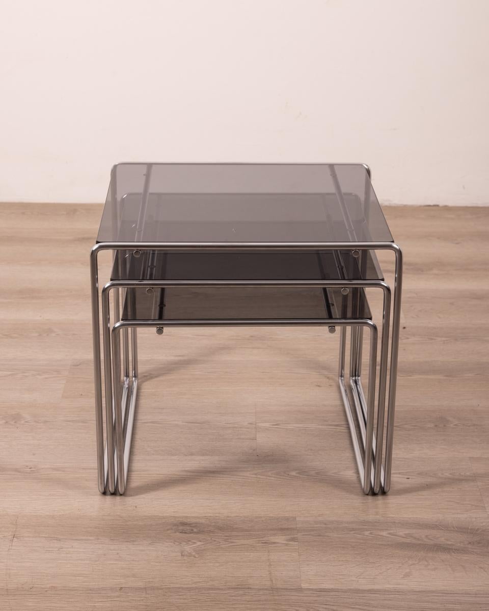 Tris di tavolini impilabili con struttura in metallo cromato e piano in vetro fumè.
Modello Marcel T, design Kazuhide Takahama per Cassina, anni 70.

CONDIZIONI: In buone condizioni, può presentare segni d'usura dati dal tempo.

DIMENSIONI: Altezza