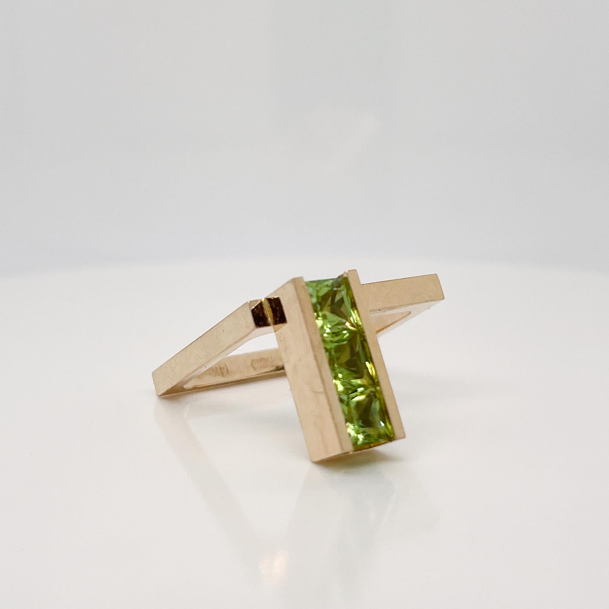 A very fine signed gold and tourmaline cocktail ring.

By Trisko. 

In 14k yellow gold. 

The ring square-shaped with an offset rectanglar head (set to the right side).

Channel set with three faceted, princess cut green tourmaline