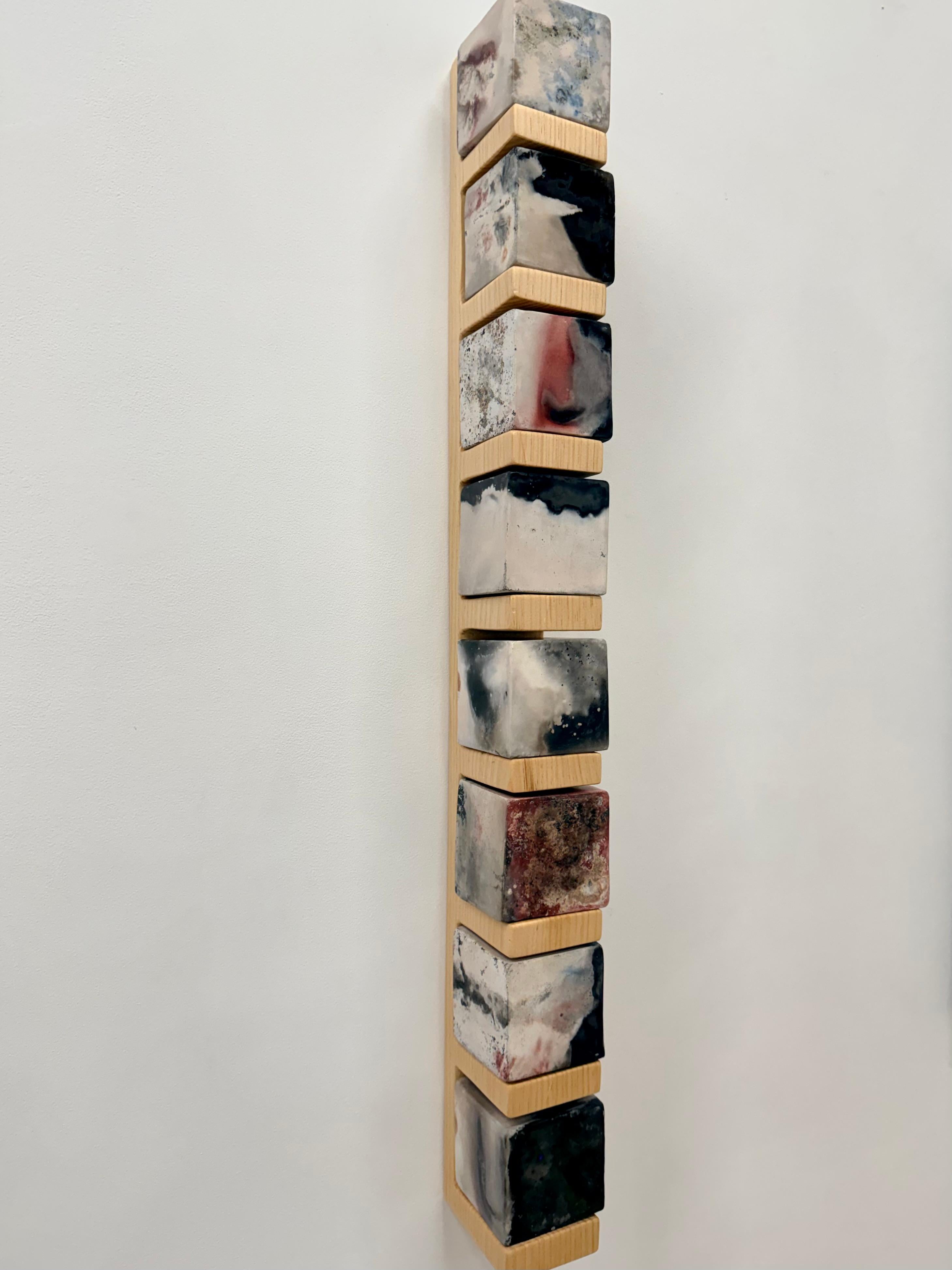 Scultura contemporanea a parete di Tristan Fitch composta da cubi di porcellana cotti in fossa su una mensola intagliata a mano in pino di provenienza locale che fa riferimento alle forme architettoniche e all'alchimia. I cubi di ceramica vengono