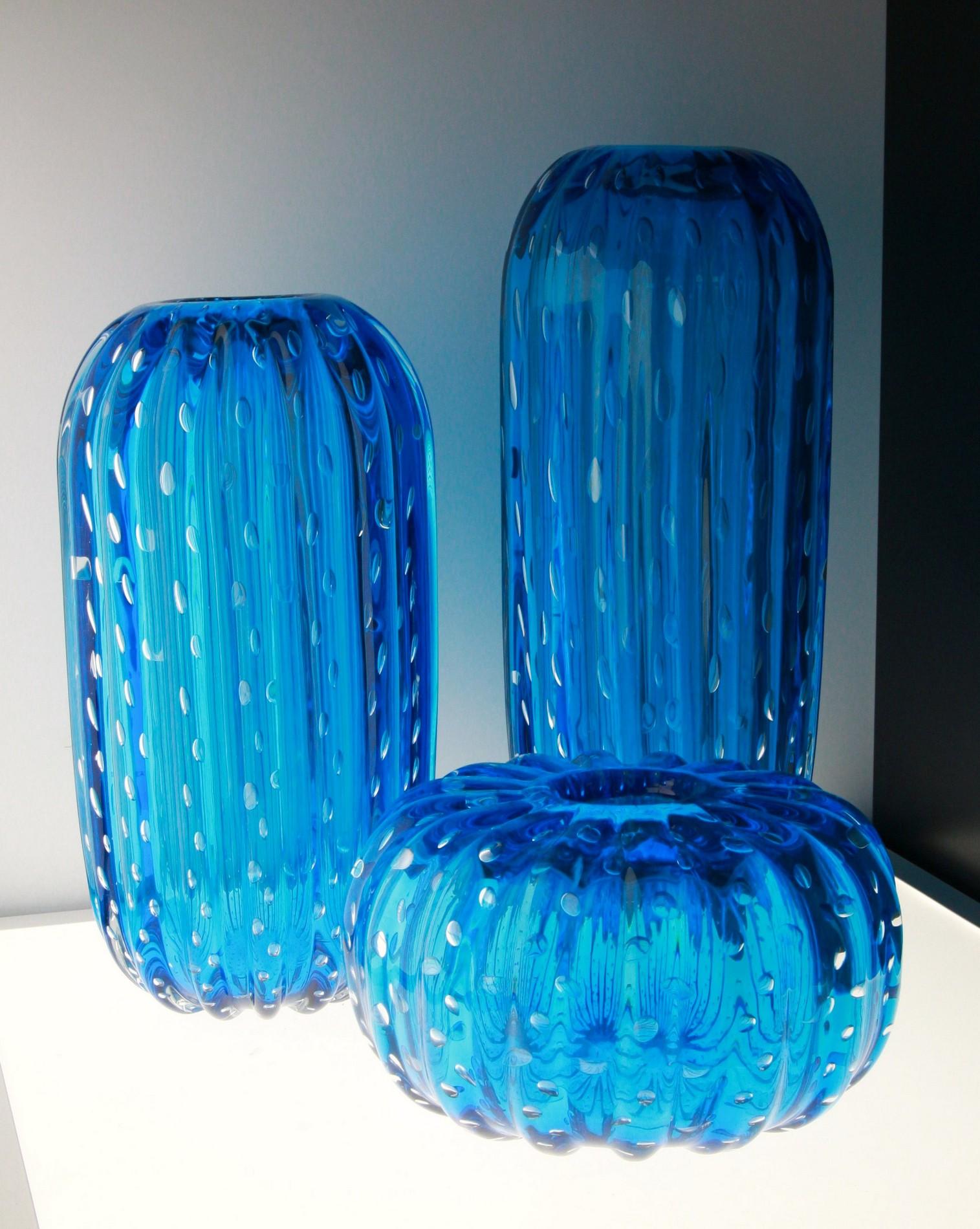 Deep acquamarine coated with clear. A vibrant group of three vases made combining the regarding straight technique and the baloton. Shape is cylindrical and resembles the Saguaro cactus. 

Best close to a window to highlight the play of light with