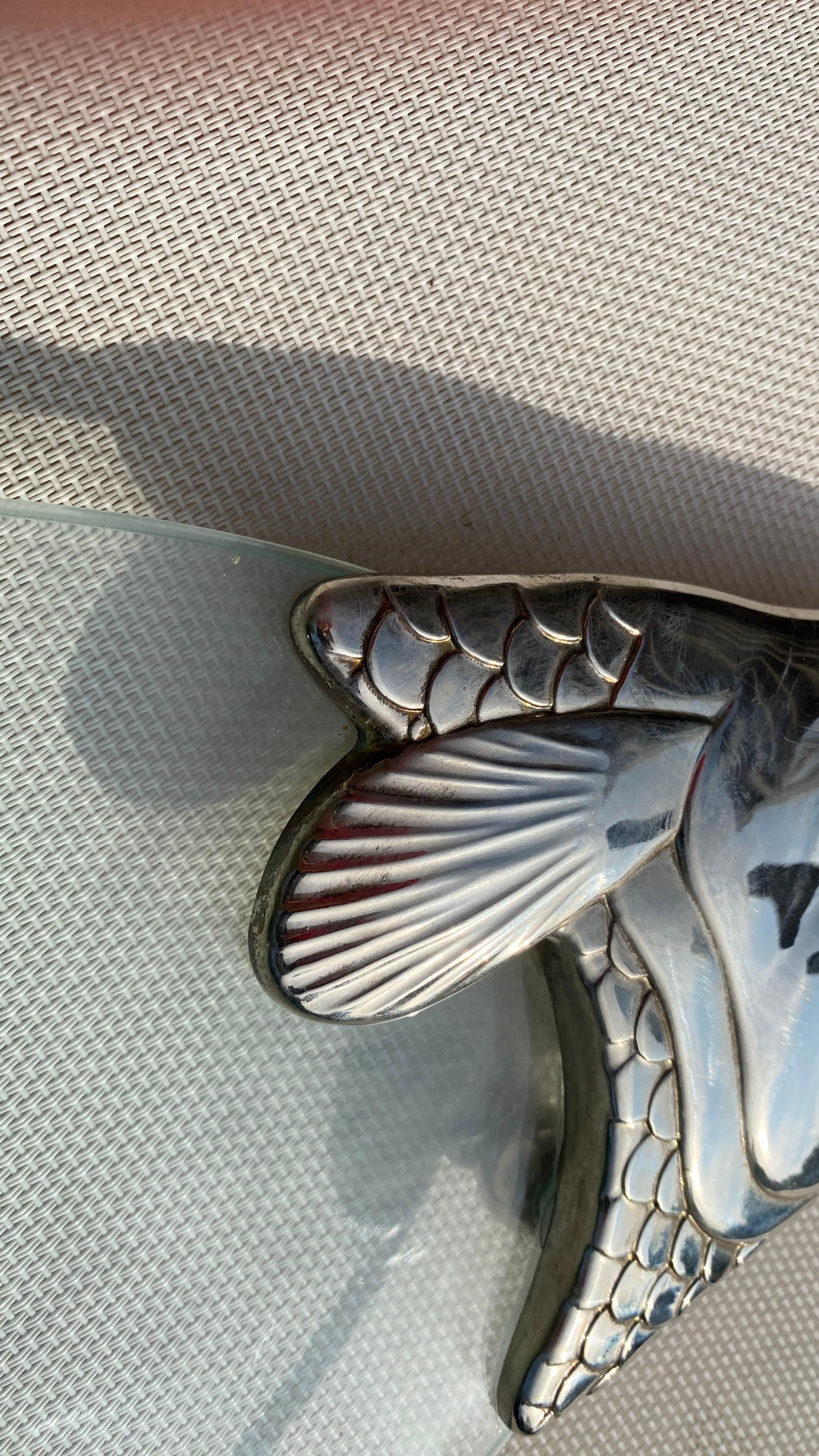 This trivet is a centerpiece in metal and glass. It has been made in France, around 1970.
The pattern is a silver fish shape.